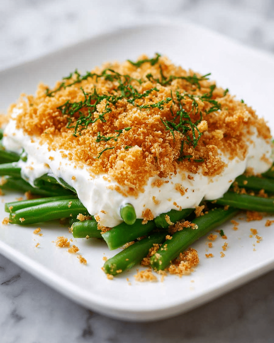 A white square plate holds a dish with three clear layers. The bottom layer is made of shiny green beans, arranged loosely and fresh looking. On top of the beans sits a thick white creamy sauce spread unevenly but covering most of the beans. The top layer is a dense pile of golden brown crispy crumbs, sprinkled with small green herb bits, adding texture and color contrast. The background surface is a white marbled texture. photo taken with an iphone --ar 4:5 --v 7