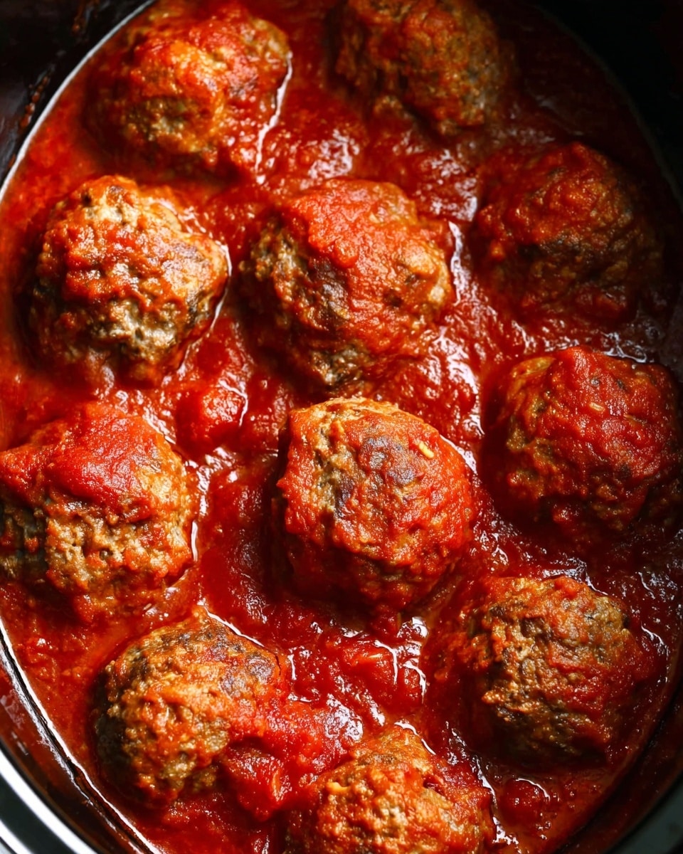 The image shows several round meatballs in a slow cooker filled with thick red tomato sauce. Each meatball has a browned, slightly crispy texture on the top and looks moist from the sauce. The sauce surrounds the meatballs evenly, with small chunks and a rich, smooth texture. The slow cooker is black on the edges, highlighting the bright red sauce and brown meat layers inside. The overall look is warm and hearty, with a close-up view that emphasizes the color contrast between the brown meatballs and vibrant red sauce. photo taken with an iphone --ar 4:5 --v 7
