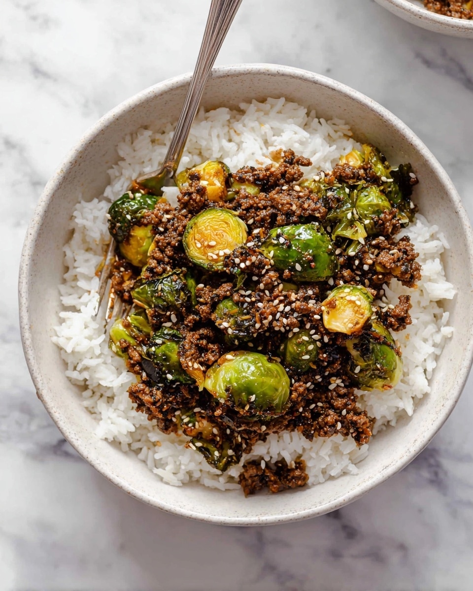 A white bowl placed on a white marbled surface holds a dish with two main layers. The bottom layer is white rice, covering the entire bowl with fluffy, separated grains. On top is a mixed layer of cooked ground meat that is dark brown and small in size, along with bright green roasted Brussels sprouts that have some crispy, browned edges. Some light-colored sesame seeds are sprinkled over the top. A silver fork is resting on the left side inside the bowl, partially dipped into the food. The photo taken with an iphone --ar 4:5 --v 7