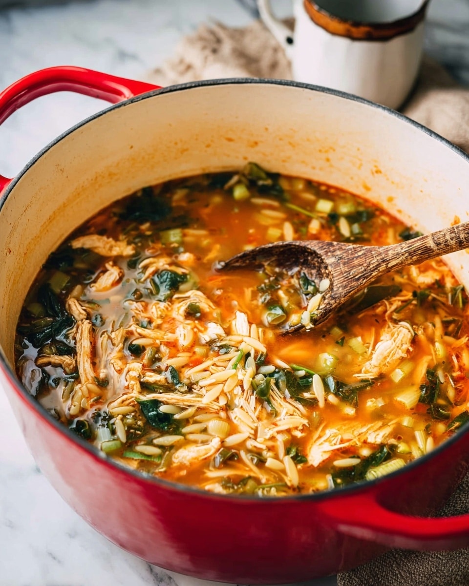 A large red pot with a white inside is filled with a colorful soup showing layers of light orange broth mixed with shredded white chicken pieces, small green and dark green leafy vegetables, and pale orange orzo pasta floating throughout. A wooden spoon with a worn look is stirring the mixture inside the pot. The pot is set on a white marbled surface with a folded beige cloth nearby and a white mug with a dark rim in the blurred background. The image has a bright, natural light feel, emphasizing the colors and textures of the soup photo taken with an iphone --ar 4:5 --v 7