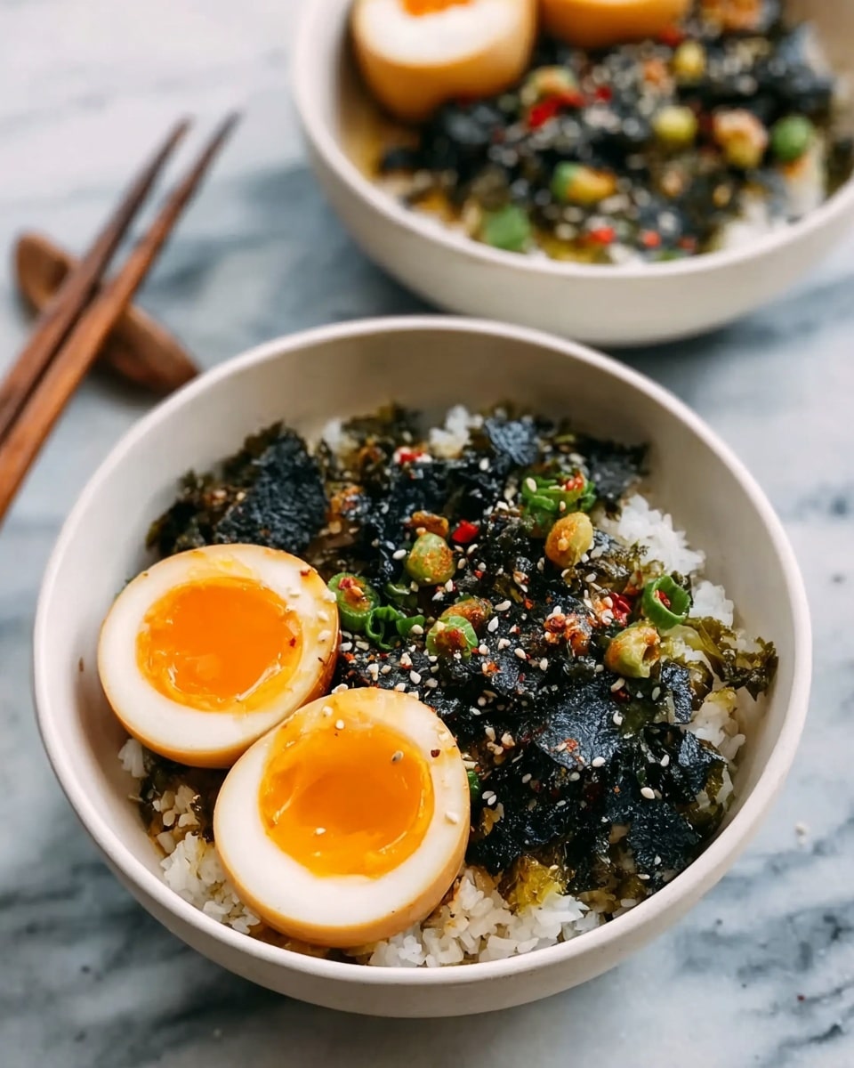 A white bowl with a base layer of white rice that looks soft and slightly sticky. On top of the rice, there is a layer of dark, crinkly seaweed pieces scattered around. Two halves of a soft boiled egg with a shiny orange yolk sit on one side of the bowl, sprinkled lightly with sesame seeds and small green and red vegetable bits. In the background, another white bowl shows a similar setup with more halved eggs and mixed veggies. Both bowls are on a white marbled surface with a pair of wooden chopsticks beside them. photo taken with an iphone --ar 4:5 --v 7