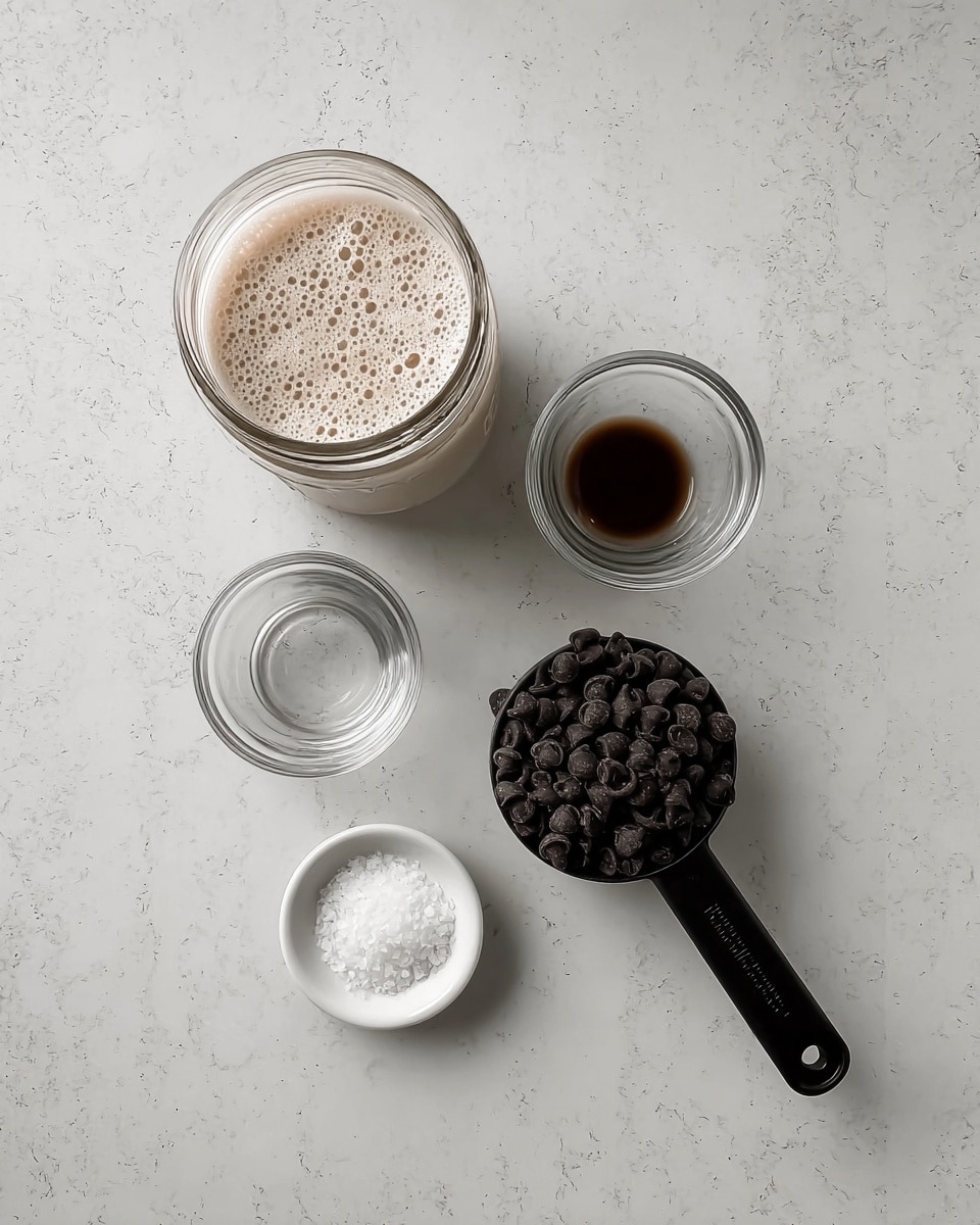 The image shows five items on a white marbled surface. At the top left is a glass jar filled with a foamy light beige liquid. To its right is a small clear glass container with a small amount of dark brown liquid. Below the jar, slightly left, is an empty small clear glass container. To the right of that, near the bottom right corner, is a black measuring cup full of dark chocolate chips. Below these items is a small white dish holding a small pile of white salt. The layout is neat and evenly spaced. Photo taken with an iphone --ar 4:5 --v 7