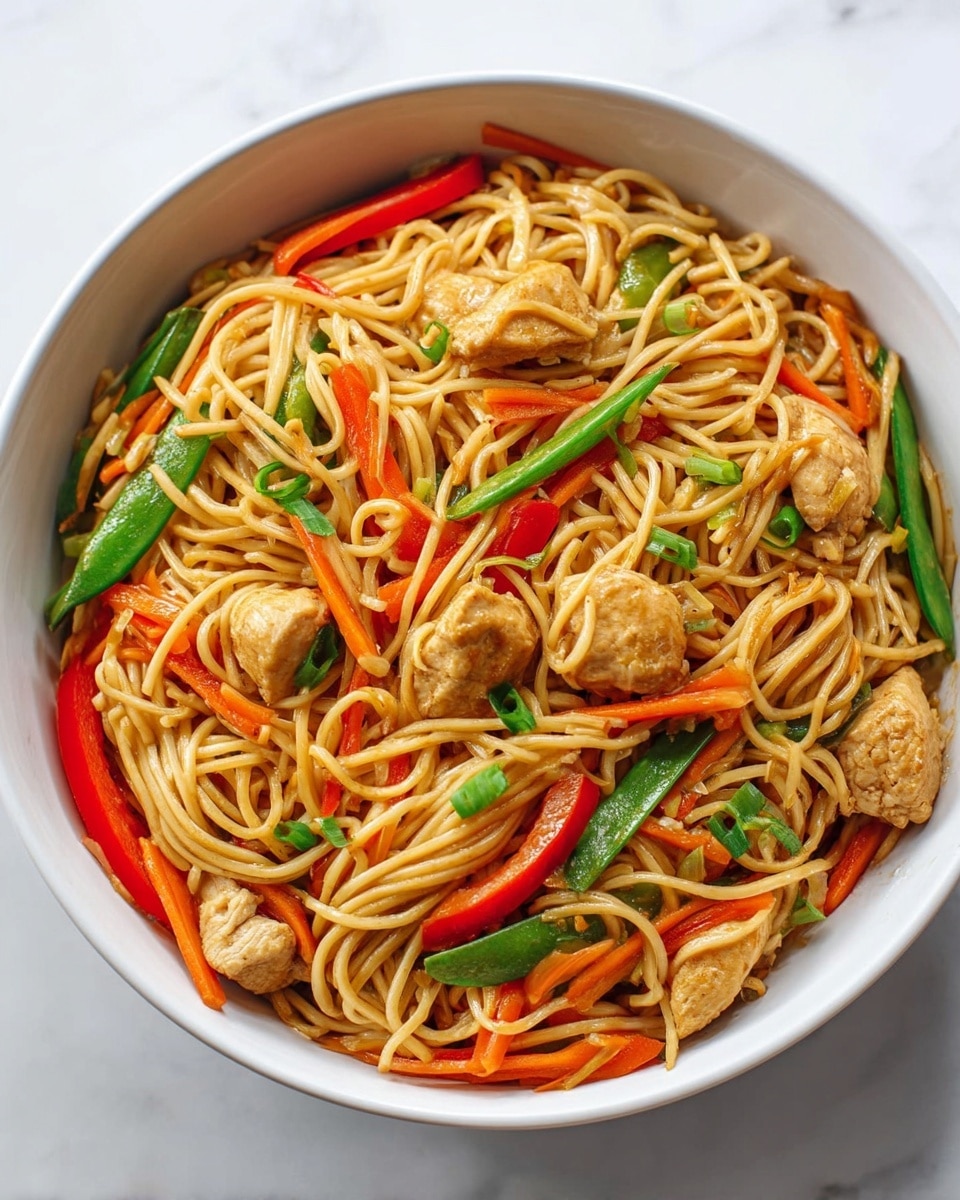 A white round bowl filled with stir-fried noodles that form a loose tangle covering the whole bowl. Mixed throughout are small, light brown pieces of cooked chicken, bright orange carrot sticks, red bell pepper strips, and green snap peas. The dish is sprinkled with small green onion pieces, all sitting on a white marbled surface. photo taken with an iphone --ar 4:5 --v 7
