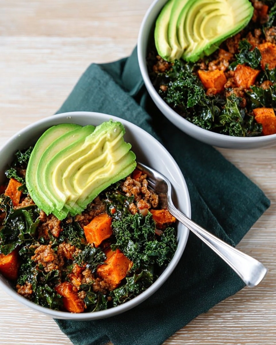 Two white bowls filled with a dish that has three layers: the bottom layer is cooked dark green leafy kale with a slightly wrinkled texture, the middle layer is orange chunks of cooked sweet potato mixed with browned ground meat, and the top layer is thinly sliced light green avocado fanned out on one side. One white bowl has a silver fork placed inside it, resting on a dark green cloth napkin. The bowls are placed on a light wooden surface. Photo taken with an iphone --ar 4:5 --v 7