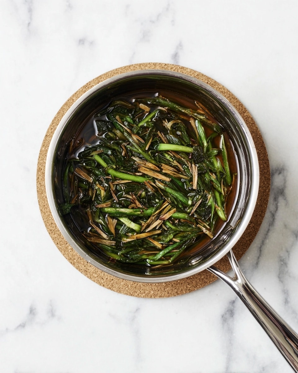 A silver metal saucepan filled with a mixture of cooked green vegetables and thin brown strips, all sitting in a dark, oily liquid. The green vegetables appear long and soft, mixed evenly with the thin brown pieces, which look slightly crispy. The pan is placed on a round cork coaster, all set on a white marbled surface. The scene is shot from above, highlighting the textures and colors inside the pan, photo taken with an iphone --ar 4:5 --v 7