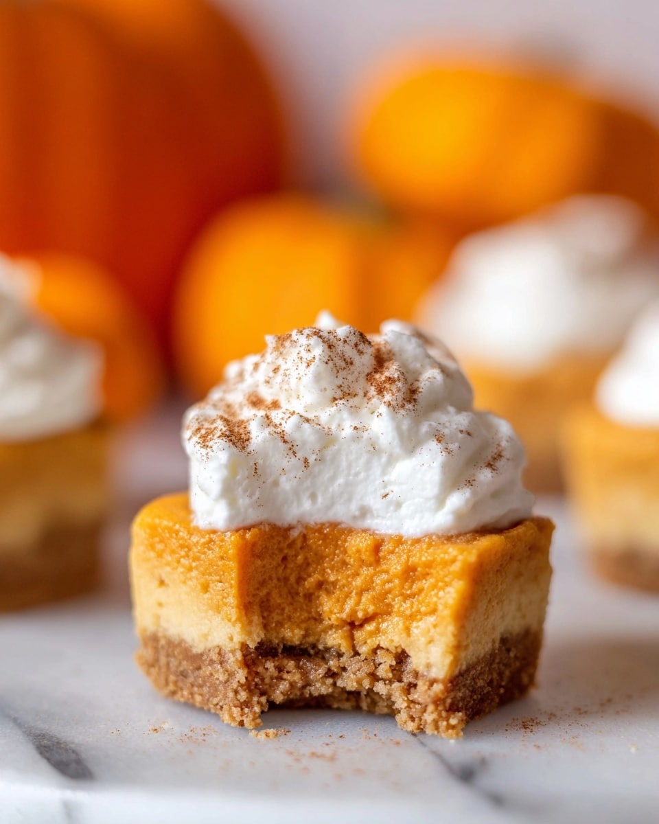A close-up image of a small pumpkin dessert with three distinct layers: the bottom layer is a light brown crumbly crust, the middle layer is a thick, smooth orange pumpkin filling, and the top layer is a fluffy white whipped cream dollop sprinkled with fine brown cinnamon powder. The dessert is sitting on a white marbled surface, with blurred orange pumpkins and more whipped cream in the background for a soft, warm ambiance. The dessert shows a bite taken out, revealing the texture of the filling and crust inside. Photo taken with an iphone --ar 4:5 --v 7