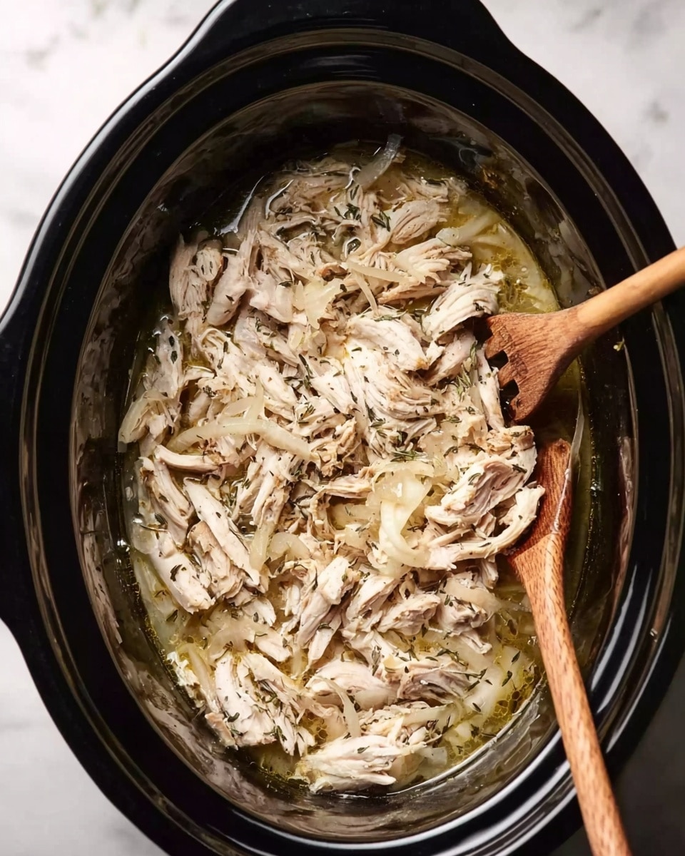 Inside a black slow cooker, there is a single layer of shredded cooked chicken mixed with translucent cooked onion slices and herbs, all sitting in a light golden broth that fills some gaps between the chicken pieces. Two wooden-handled forks rest diagonally on the right side of the slow cooker, partially touching the chicken. The slow cooker is placed on a white marbled surface. photo taken with an iphone --ar 4:5 --v 7