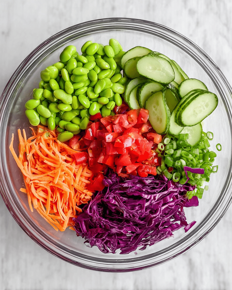 A clear glass bowl holds five neat sections of fresh vegetables arranged in a circle. Starting from the top, bright green edamame beans form a rounded pile. To the right, thinly sliced cucumber rounds with dark green edges overlap slightly. Below the cucumbers, chopped red tomatoes create a bright red section. Next to the tomatoes, thin orange carrot sticks fill the space. Finally, shredded deep purple cabbage sits opposite the carrots, with small slices of green scallions next to it. The bowl is placed on a white marbled surface. photo taken with an iphone --ar 4:5 --v 7