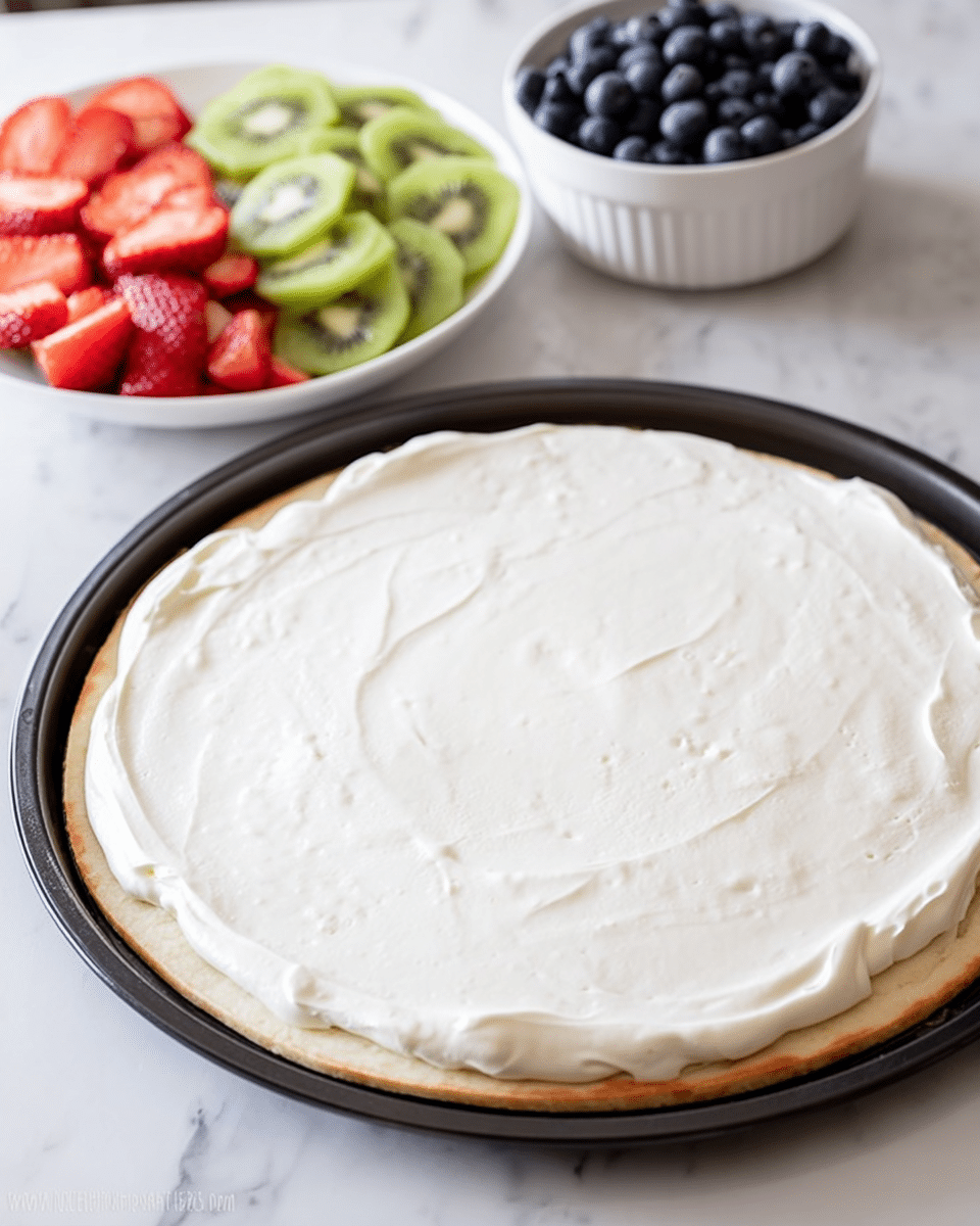 A large round flat dough base is spread with a smooth, thick white cream layer that covers the entire surface evenly, sitting on a black pizza pan on a white marbled surface. In the background, there is a white bowl filled with neatly sliced layers of bright red strawberries and green kiwi arranged side by side. Nearby, a small white bowl holds fresh plump blueberries, adding a deep blue color to the scene. The image is fresh and clean with soft daylight highlighting the textures of the cream and fruit, photo taken with an iphone --ar 4:5 --v 7