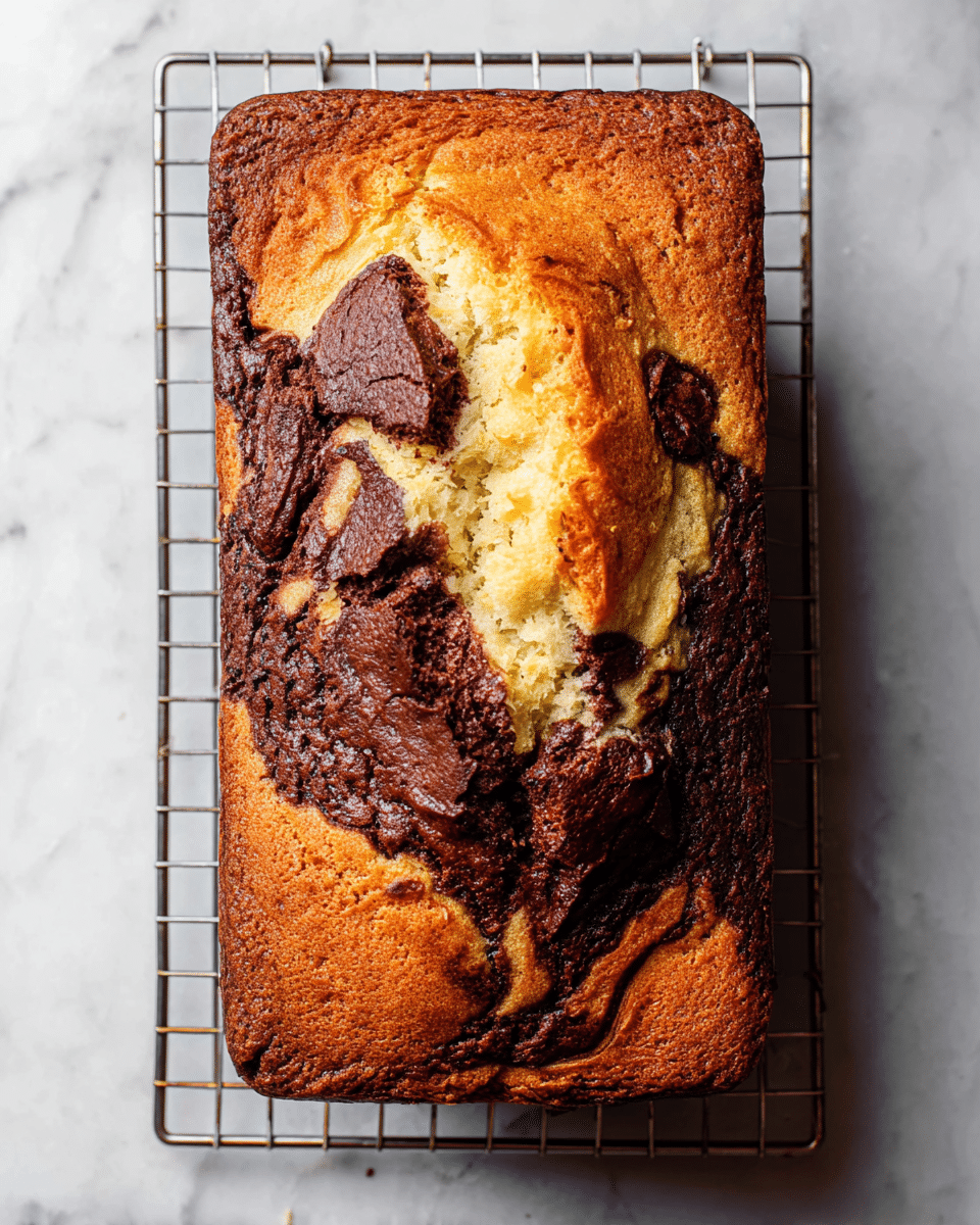 A rectangular loaf with a cracked top showing two main layers: a golden brown layer with a slightly rough, baked texture and a rich dark brown layer swirled through it, creating a marbled effect. The loaf is placed on a small metal cooling rack set on a white marbled surface. The edges of the loaf are darker, indicating a crisp outer crust, while the center looks soft and fluffy with the dark swirls embedded inside. The photo taken with an iphone --ar 4:5 --v 7
