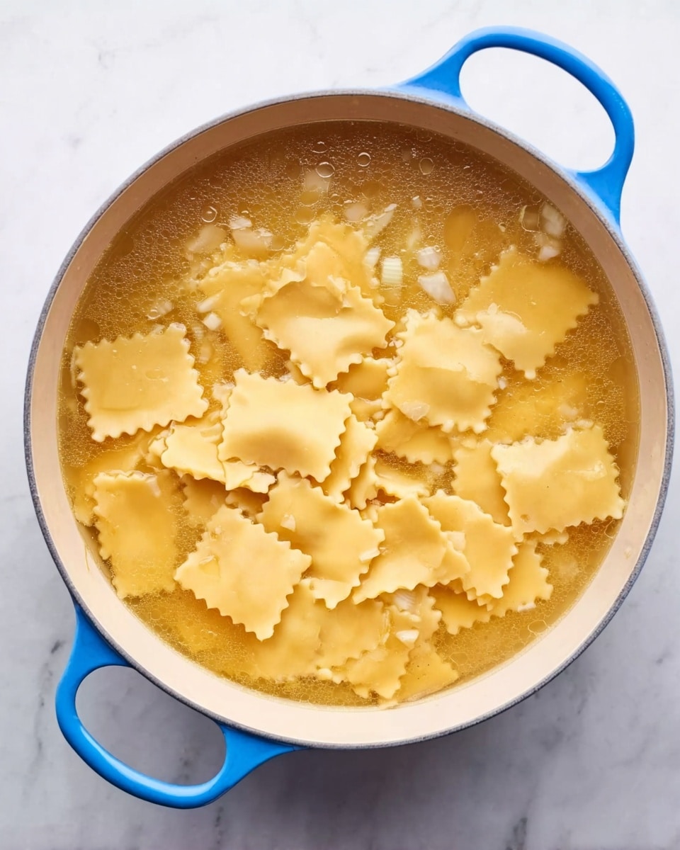 A white pot with blue handles holds light yellow square pasta pieces with wavy edges floating in a clear golden broth. Small bits of white onion are scattered on top of the broth and pasta. The pot sits on a white marbled surface, and the broth's surface has a slight shine, showing steam rising gently. The pasta pieces overlap each other and rest evenly in the broth. photo taken with an iphone --ar 4:5 --v 7