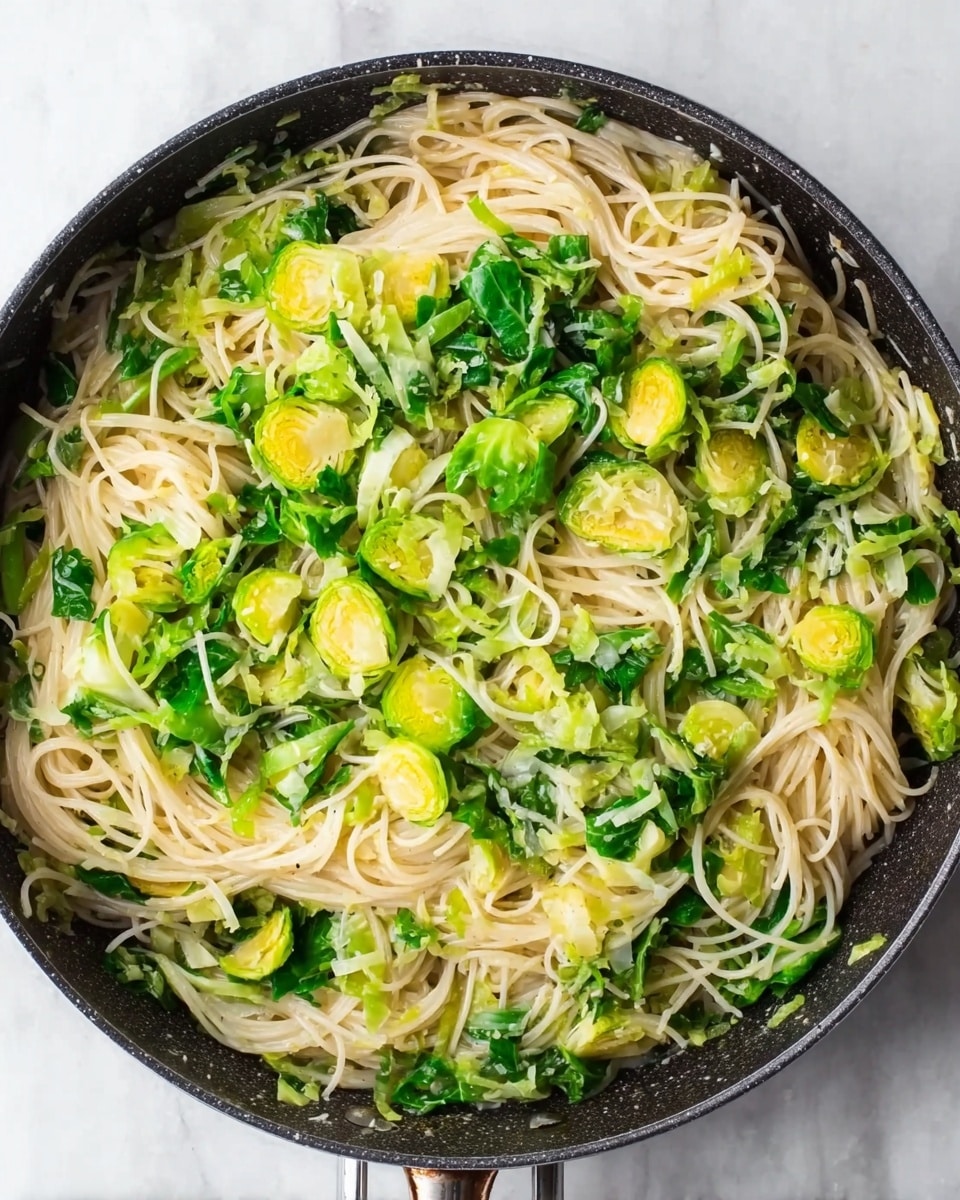 The image shows a black pan filled with thin spaghetti noodles mixed with bright green sliced Brussels sprouts and chopped leafy greens. The noodles form the base layer, spread across the pan with a light creamy texture. The Brussels sprouts slices and green leaves are scattered evenly on top, adding pops of yellow-green color and fresh texture. The pan sits on a white marbled surface, enhancing the fresh and simple look of the dish. photo taken with an iphone --ar 4:5 --v 7