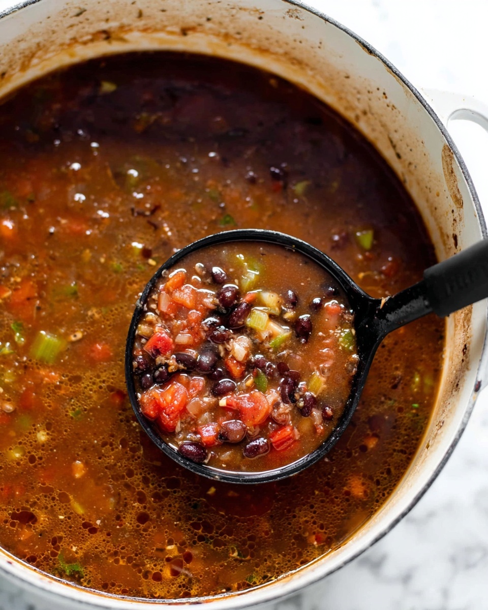 Creamy Black Bean Soup with Fresh Toppings Recipe 5 A close-up view of a large white pot filled with dark brown soup that has a slightly oily surface and small bubbles around the edges. Inside the soup, there are visible chunks of red tomatoes, black beans, green celery, and bits of onion, all mixed through the rich broth. A black ladle is scooping a portion of the soup, showing a mix of the vegetables and beans clearly against the liquid. The pot has some splattered soup marks around the rim, and it is placed on a white marbled surface. photo taken with an iphone --ar 4:5 --v 7