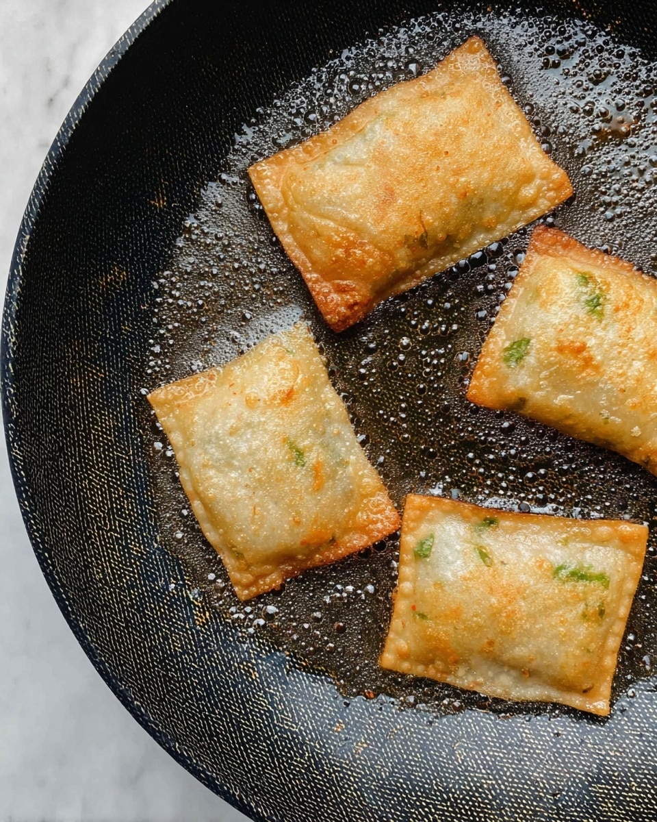 Four small golden-brown square pockets with a light crispy texture are cooking in a black frying pan with a patterned non-stick surface, with visible bubbles on their surface showing they are frying in oil that glistens along the edges of the pan; the pockets have some green and orange spots inside the translucent wrapper showing the filling. The pan sits on a white marbled surface. photo taken with an iphone --ar 4:5 --v 7