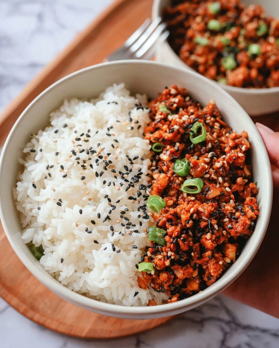 A white bowl filled with two main layers side by side: on the left, fluffy white rice with separated grains, and on the right, a reddish-brown minced dish sprinkled with black and white sesame seeds and small sliced green onions, showing a slightly chunky texture. The bowl is placed on a wooden surface with a white marbled texture visible around. In the background, there is a similar bowl slightly out of focus with the same dish. A metal fork is placed nearby, and a woman's hand is softly holding the bowl. photo taken with an iphone --ar 4:5 --v 7