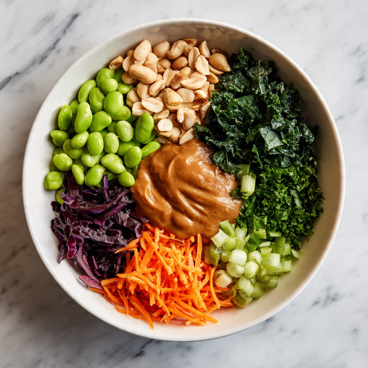 A white bowl holds a colorful salad arranged in layers from above. On one side, bright green edamame beans form a smooth, shiny layer. Next to it, light beige peanuts add a rough texture. Above the peanuts, dark green kale leaves create a leafy, textured layer. To the right of the kale, finely chopped fresh green herbs provide a delicate, small-leaf texture. Below the herbs are thin slices of light green scallions. Next to them is a layer of chopped dark purple cabbage with a crisp look. Below that, a pile of shredded bright orange carrots adds a soft, stringy texture. A large dollop of thick, smooth brown sauce covers the middle right part of the bowl, partially covering some vegetables. The bowl sits on a white marbled surface. Photo taken with an iphone --ar 4:5 --v 7