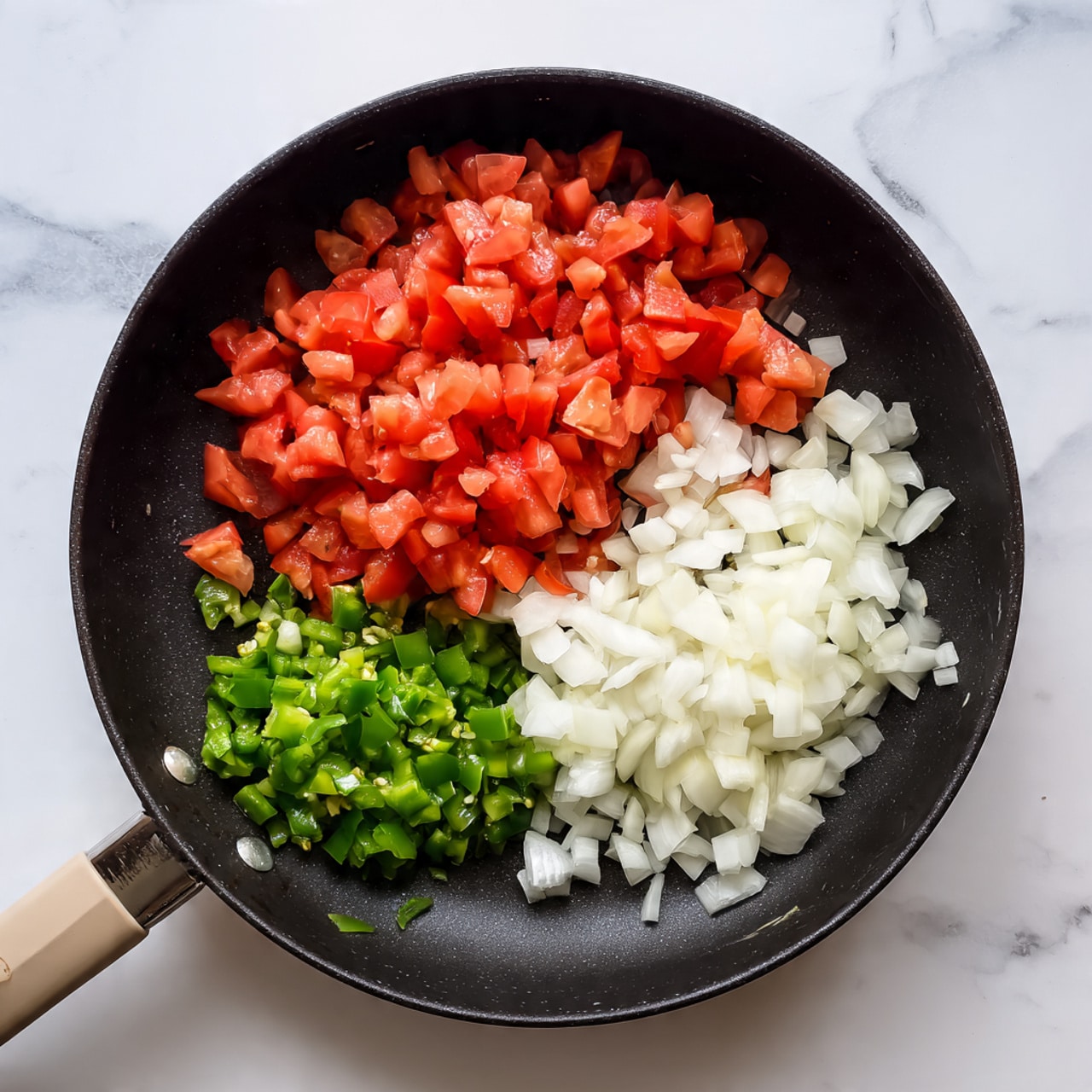 Inside a black frying pan on a white marbled surface, there are three piles of chopped ingredients arranged close to each other. On the top right is a pile of white onions with a slightly glossy texture. To the left of the onions is a bigger pile of red tomatoes, diced into small cubes with a juicy and fresh look. Below the onions and tomatoes is a small pile of chopped green chili peppers, bright and smooth in texture. The frying pan has a light-colored handle that rests on the surface, and the lighting makes the colors of the ingredients look clear and fresh. photo taken with an iphone --ar 4:5 --v 7