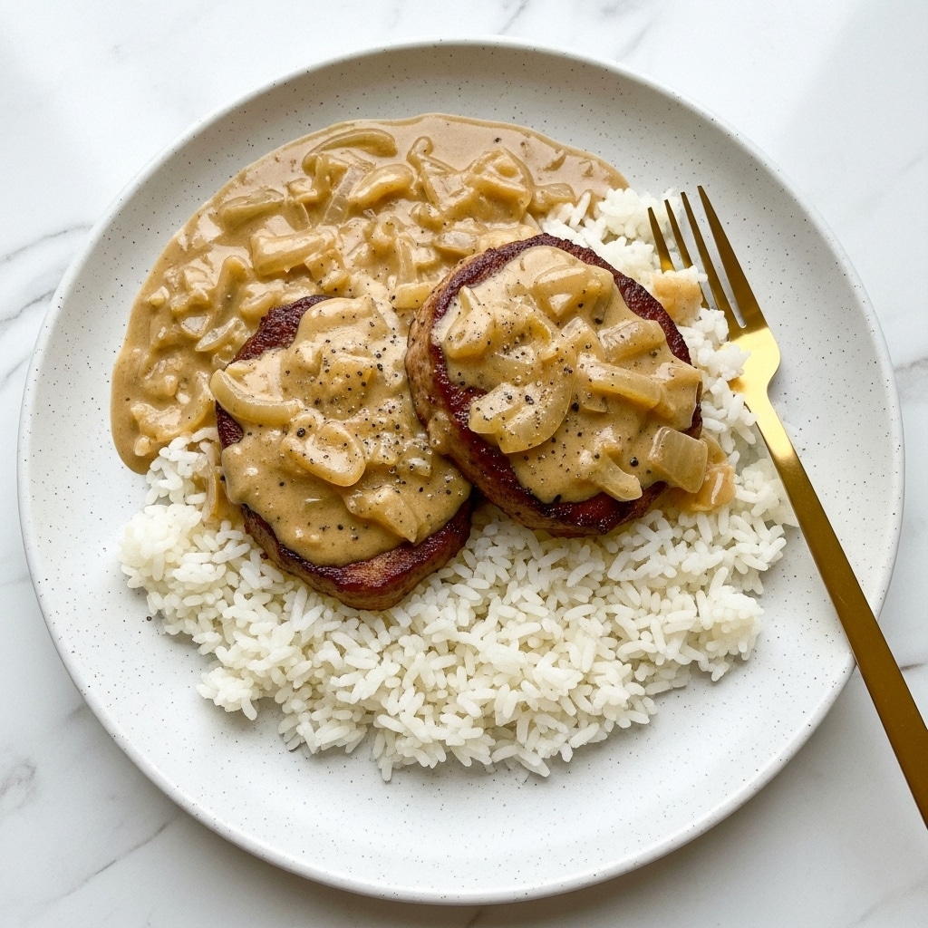 A metal pan filled with three thick pieces of browned meat, partially covered in a smooth, glossy light brown sauce with visible small bits, likely onions. A wooden spoon with a curved edge rests inside the pan on the right side, partially dipped in the sauce. The pan sits on a white marbled surface, and the sauce has a creamy texture with some darker spices sprinkled throughout photo taken with an iphone --ar 4:5 --v 7