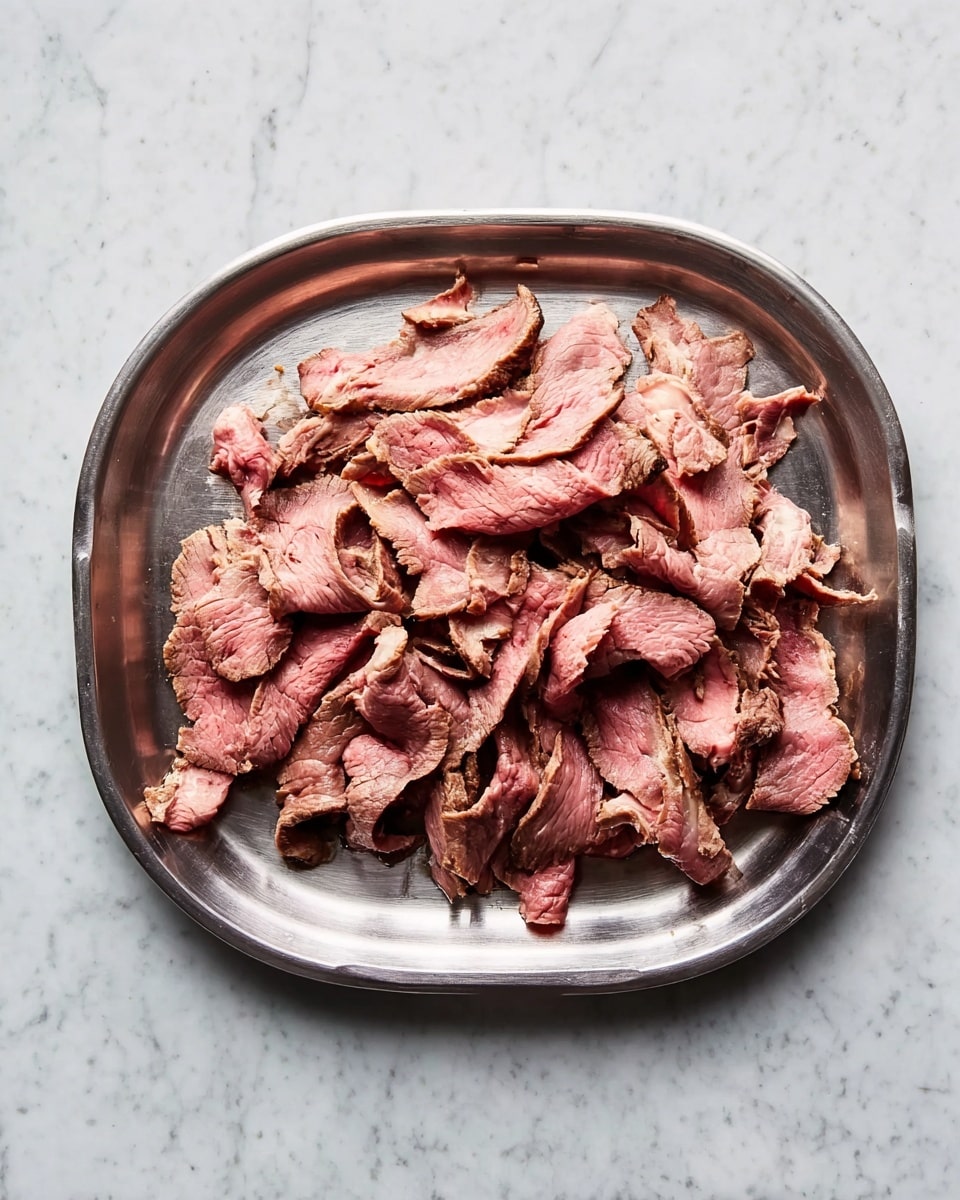 A metal tray holds thin slices of cooked beef arranged loosely in the center. The beef layers show a mix of pink and brown colors, with the pink indicating the inside and the brown on the edges. The texture of the meat appears soft and tender with some slight folds and curves. The tray rests on a white marbled surface. photo taken with an iphone --ar 4:5 --v 7