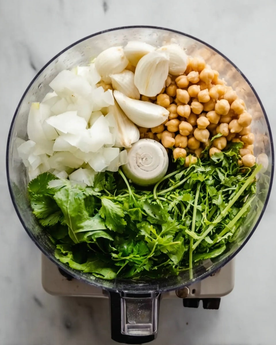 A top-down view of a clear food processor bowl filled with several layers of fresh ingredients. On one side, bright green leafy herbs with fine stems create a fresh texture. Next to them, several whole garlic cloves are smooth and white, sitting close to small round chickpeas with a pale golden color. On the opposite side, thick white chunks of onion add a crisp and solid layer. All ingredients are arranged together, placed on a white marbled surface. Photo taken with an iphone --ar 4:5 --v 7