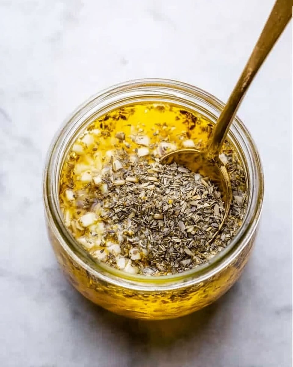 A clear glass jar filled with multiple layers is shown from above on a white marbled surface. The bottom layer consists of small chopped white and light brown pieces, topped with a thick layer of yellowish liquid. On top of that, there is a dense sprinkle of dried herbs or seeds, grayish and finely textured. A brass spoon partly dipped into the jar's contents rests at an angle inside it. The jar itself is round and transparent, showing all contents clearly, making the layers stand out. photo taken with an iphone --ar 4:5 --v 7
