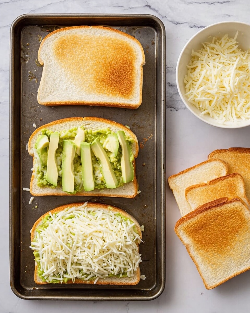 The image shows a baking tray with four sandwich slices; three of them have a golden toasted bottom layer with mashed avocado spread on top, one with thinly sliced avocado pieces neatly arranged over the mash, and another with a generous amount of shredded white cheese covering the avocado layer. One slice remains with the plain top layer of white bread ready to cover the filled slices. On the top right is a small white bowl filled with more shredded white cheese, and on the bottom right are two lightly toasted white bread slices resting on a white marbled surface. photo taken with an iphone --ar 4:5 --v 7