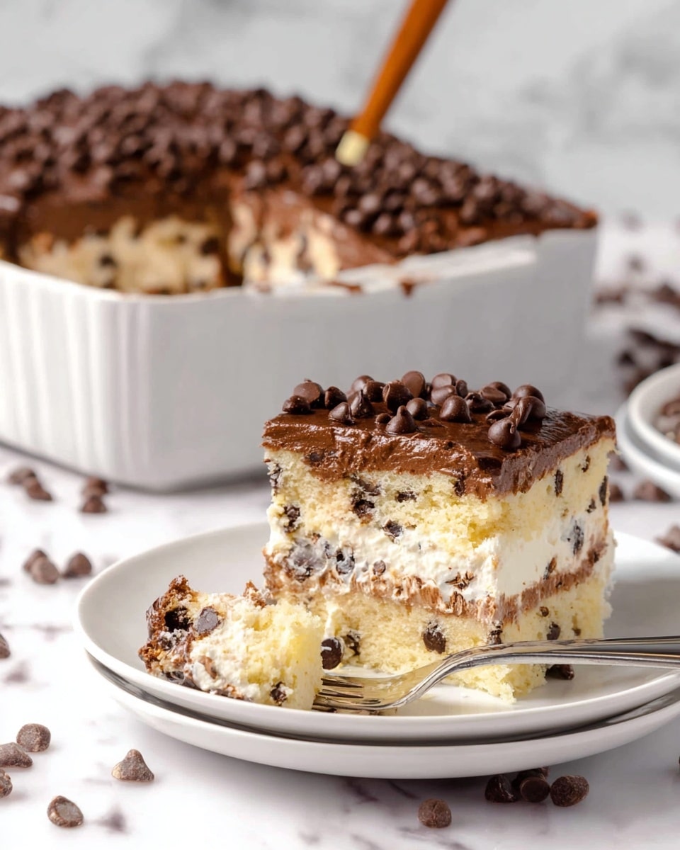 A close-up of a layered cake slice on a white plate with a silver fork holding a bite, showing three main layers: a light yellow cake mixed with small dark spots of chocolate chips at the bottom, a thick white creamy layer with chocolate chips in the middle, and a thick dark chocolate frosting layer on top sprinkled with many chocolate chips. Behind it, there is a white dish with the rest of the layered cake inside, and a utensil with a wooden handle is resting inside the dish. The scene is set on a white marbled surface with scattered chocolate chips around. Photo taken with an iphone --ar 4:5 --v 7