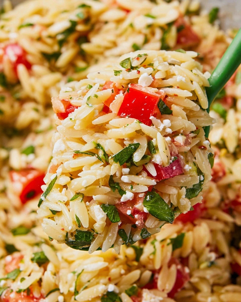 A close-up view of a spoon full of orzo pasta salad with three main layers: the first layer consists of small oval-shaped orzo pasta that is light yellow with a slightly shiny texture; the second layer has small pieces of bright red tomatoes cut into cubes scattered evenly; the third layer shows chopped green herbs and small bits of white cheese crumbled lightly throughout the mix. The background is a white marbled texture with more of the orzo pasta salad visible, showing the same elements mixed together. The spoon is green and held by a woman's hand, lifting the salad up. Photo taken with an iphone --ar 4:5 --v 7