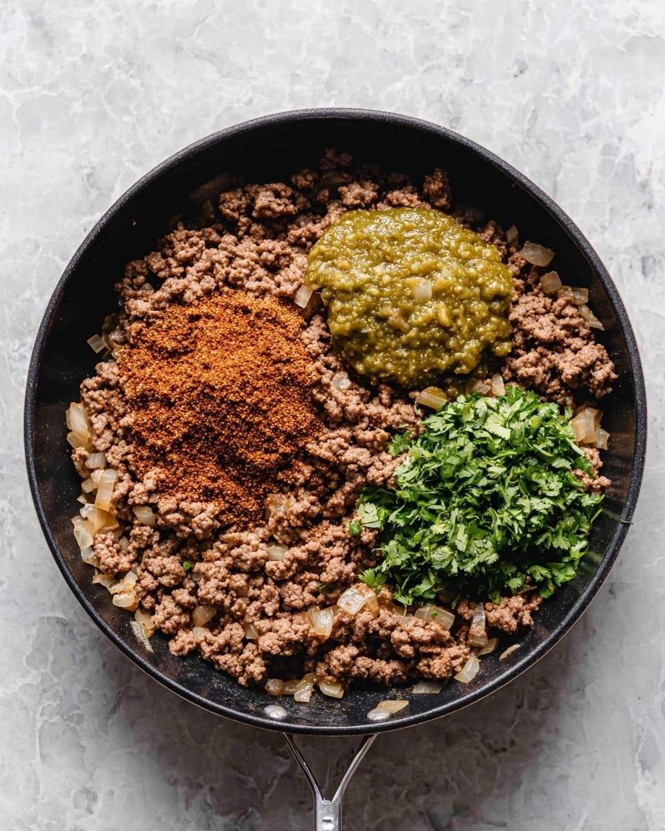 A black skillet filled with cooked, crumbled ground beef mixed with small pieces of cooked onions as the base layer, spread evenly across the pan. On top, there are three distinct piles: a heap of reddish-brown taco seasoning powder in the center-left, a scoop of chunky green salsa next to it on the upper right, and a small pile of fresh, roughly chopped green cilantro leaves placed on the bottom right. The skillet sits on a white marbled surface. photo taken with an iphone --ar 4:5 --v 7