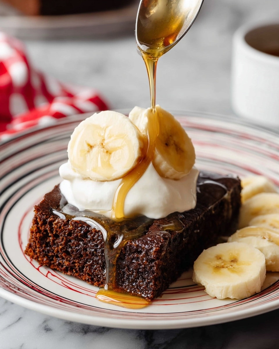 A thick dark brown slice of cake sits in the middle of a white plate with red and black lines. On top of the cake is a dollop of white whipped cream with two banana slices placed on it. A spoon pours light golden syrup down over the whipped cream and cake, with syrup dripping down the sides. More banana slices are placed next to the cake on the right side of the plate, all against a white marbled surface. Photo taken with an iphone --ar 4:5 --v 7