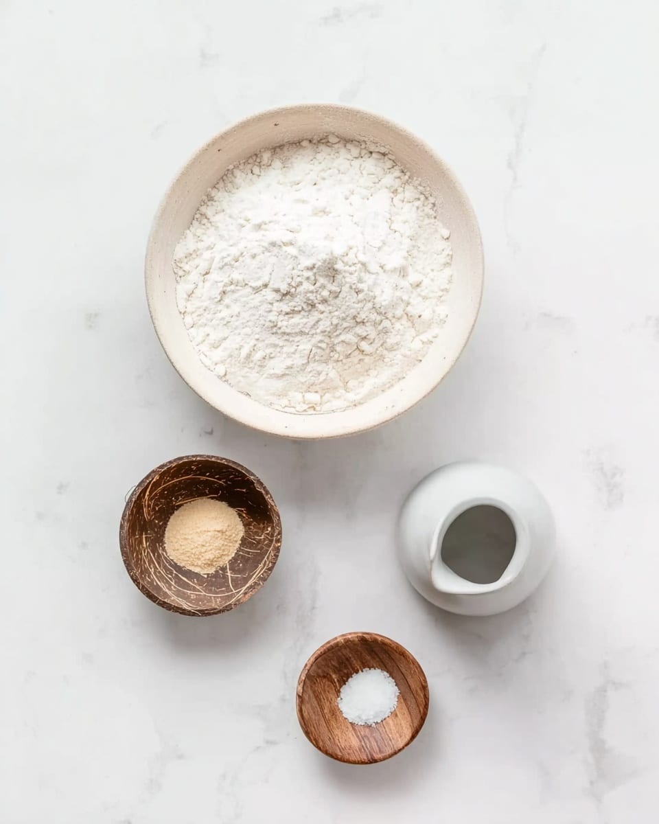 The image shows a white bowl with a light beige rim filled with white flour placed on a white marbled surface. Below the bowl, there are three small containers arranged in a triangle shape: a small coconut shell bowl with a light brown powder, a wooden bowl with white salt, and a small white jug filled with water. Everything is arranged neatly and evenly spaced on the white marbled background. Photo taken with an iphone --ar 4:5 --v 7