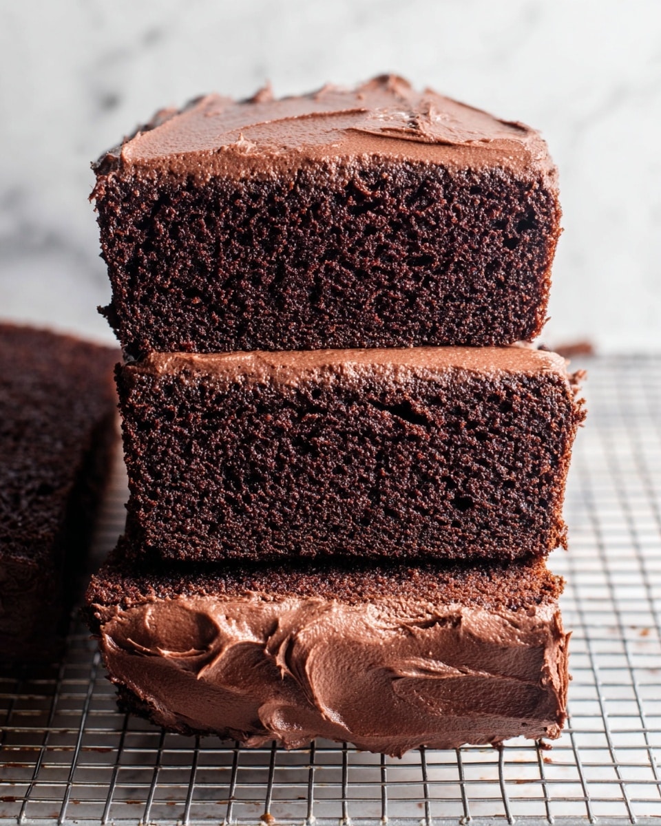 The image shows three slices of dark chocolate cake stacked on top of each other, each with a thick, smooth layer of chocolate frosting on top. The cake texture is moist and dense with small air bubbles visible. The bottom edge shows the whole cake with a thick, creamy layer of frosting spread unevenly but generously. The cake and slices are placed on a wire cooling rack over a white marbled surface. Photo taken with an iphone --ar 4:5 --v 7