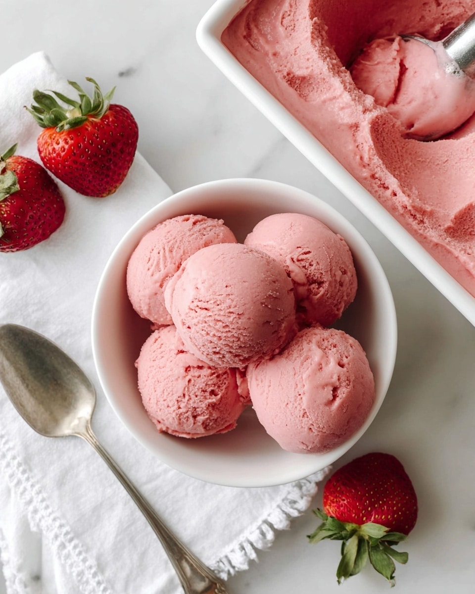 A white bowl filled with four round scoops of soft pink strawberry ice cream on a white marbled surface, beside the bowl is a silver spoon resting on a white cloth with delicate stitching; next to the bowl, there are two whole fresh strawberries with green leaves, and next to them is a white rectangular container filled with more smooth pink strawberry ice cream with a slight texture and an ice cream scoop partially visible at the top right corner photo taken with an iphone --ar 4:5 --v 7