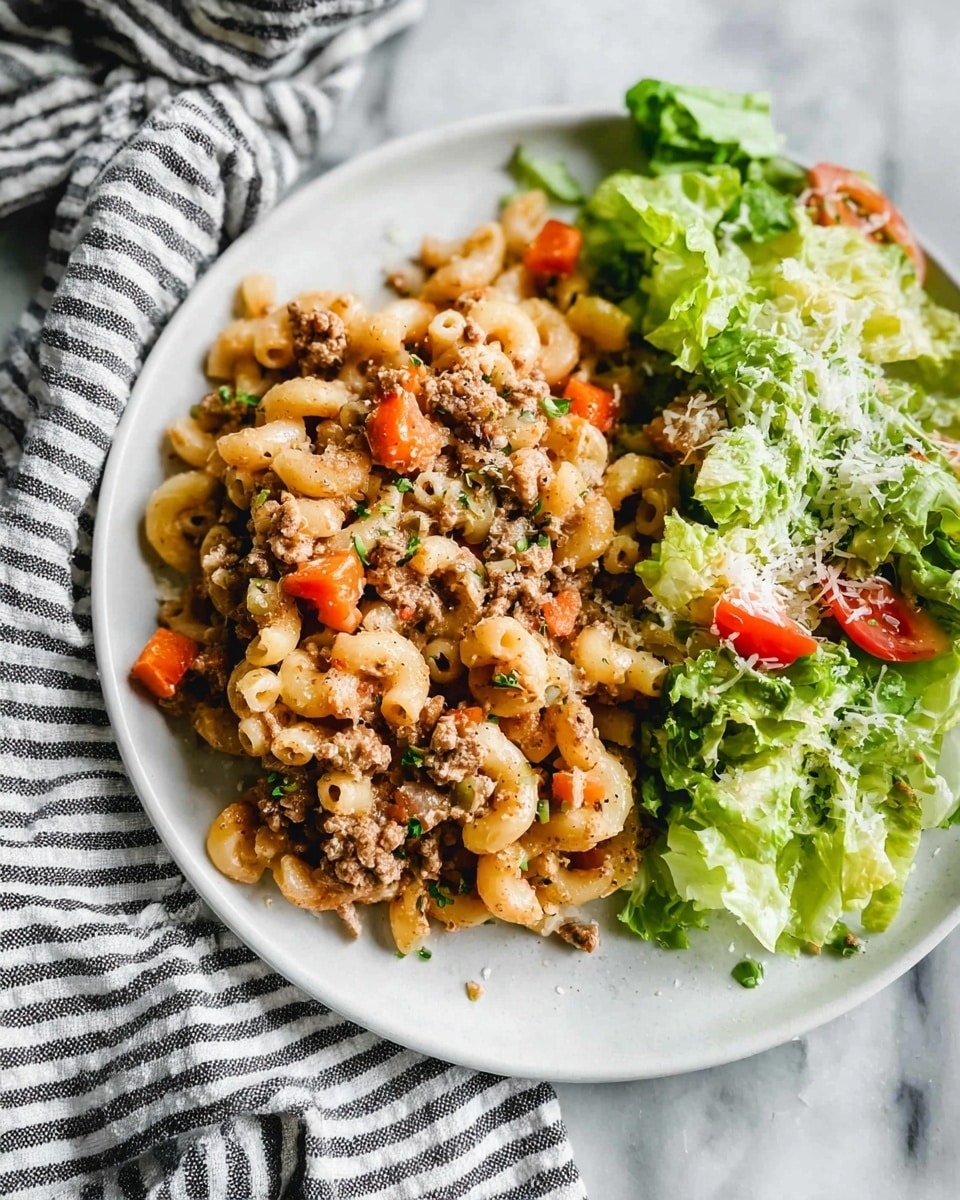 A white plate on a white marbled surface holds a dish with two main parts. The left side has elbow macaroni mixed with small chunks of cooked ground meat, diced orange carrots, and tiny green herb bits, all covered with a light sprinkling of grated cheese. The right side has fresh green lettuce leaves topped with grated cheese and small pieces of tomatoes. The plate is next to a striped cloth, and the whole scene looks bright and natural. Photo taken with an iphone --ar 4:5 --v 7