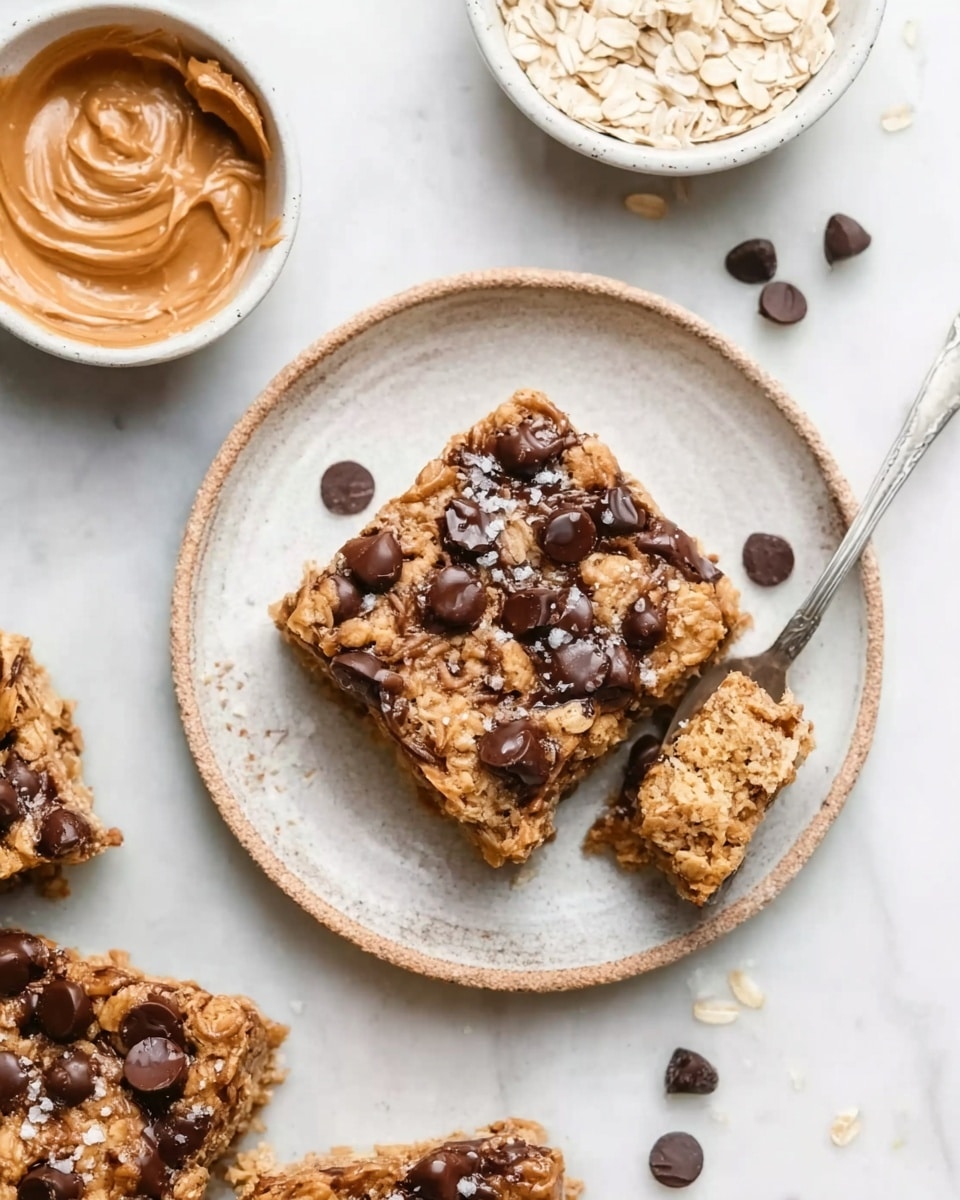 A square oatmeal bar sits on a white plate with a rough texture, filled with visible layers of oat flakes and soft baked dough. On top, there are many dark, shiny melted chocolate chips scattered across the surface, with a few flakes of white sea salt adding a touch of contrast. Around the main plate, there are small white bowls; one with raw oat flakes and another with smooth light brown peanut butter, all set on a white marbled surface. A silver spoon is lifting the oatmeal bar slightly from the plate. The colors are warm and natural, with beige oats, rich dark chocolate, and light brown peanut butter. photo taken with an iphone --ar 4:5 --v 7