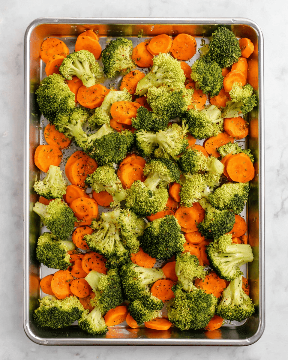The image shows a silver baking tray filled with a single layer of fresh vegetables spread out evenly. The vegetables include bright green broccoli florets with a rough, bumpy texture and vibrant orange carrot slices that are round and smooth. Both vegetables are sprinkled lightly with herbs and spices, giving them a speckled appearance. The tray is placed on a white marbled surface, creating a clean and fresh background. photo taken with an iphone --ar 4:5 --v 7