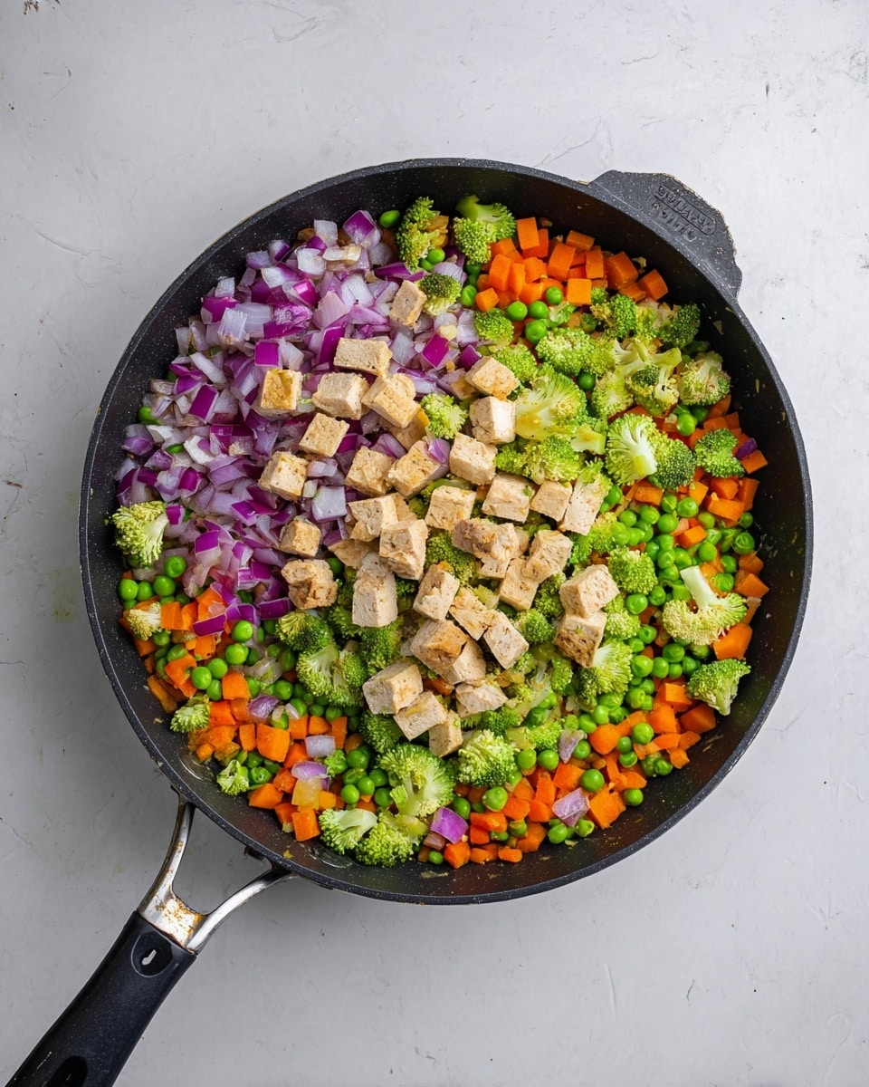 A black pan filled with a mix of chopped vegetables and tofu pieces is placed on a white marbled surface. The dish has four visible layers: the bottom layer is a mix of small, bright green peas and bits of chopped orange carrot spread evenly. The next layer includes small, vivid green broccoli florets scattered throughout. Above that, there are finely chopped purple and white onion pieces mixed all over. On top, there are several chunks of light tan tofu distributed evenly. The pan has a long handle extending to the left and a smaller handle on the right side. photo taken with an iphone --ar 4:5 --v 7