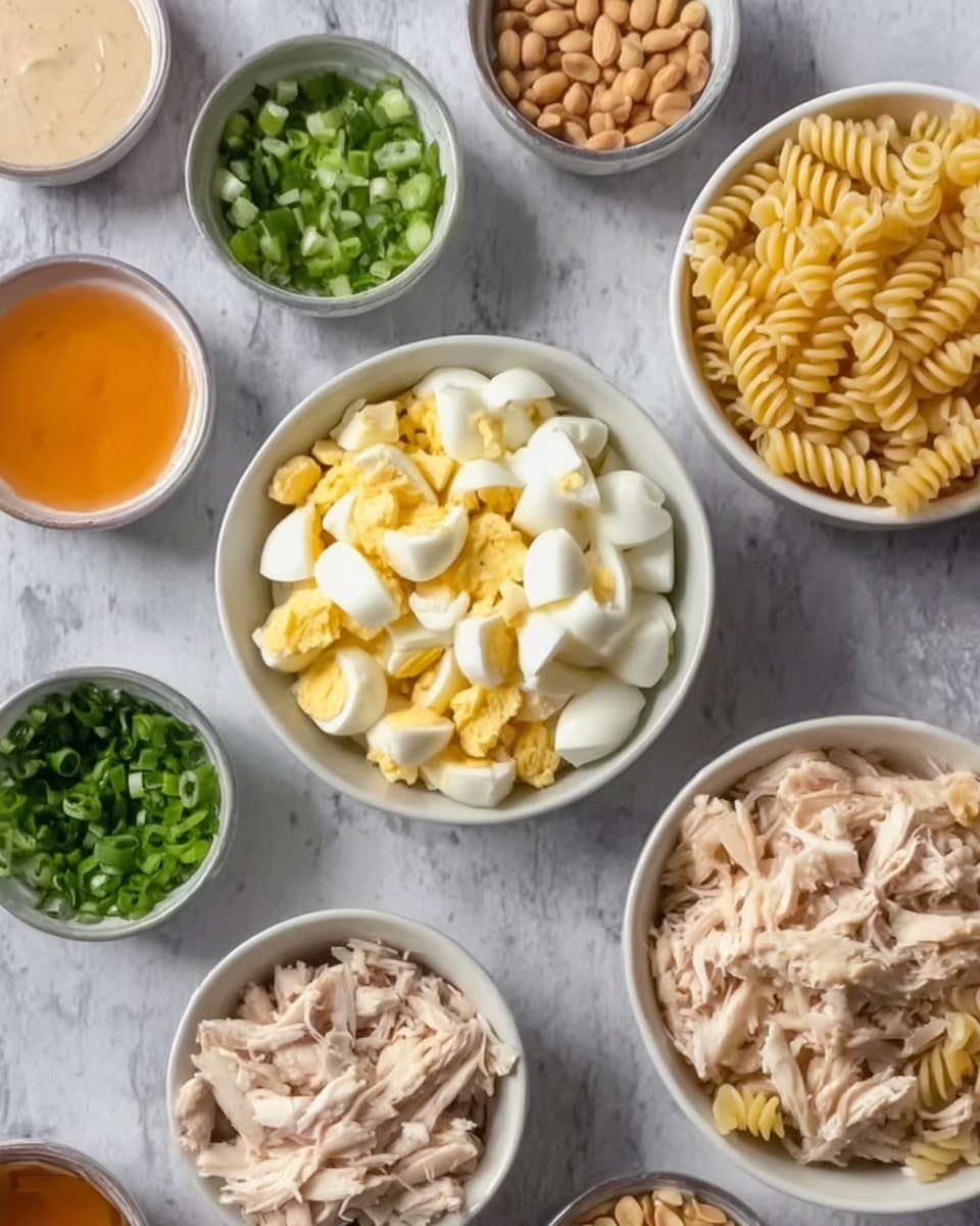 The image shows several small white bowls arranged on a white marbled surface. One bowl contains spiral-shaped pasta with a light yellow color and a ridged texture, placed on the right side. A bowl in the center holds chopped hard-boiled eggs with white and yellow pieces. Another bowl at the bottom contains shredded cooked chicken that is pale beige. Other smaller bowls around these contain finely chopped green onions, green herbs, whole peanuts, a light creamy sauce, and two liquid sauces, one orange and one white, in a bowl side by side. Photo taken with an iphone --ar 4:5 --v 7
