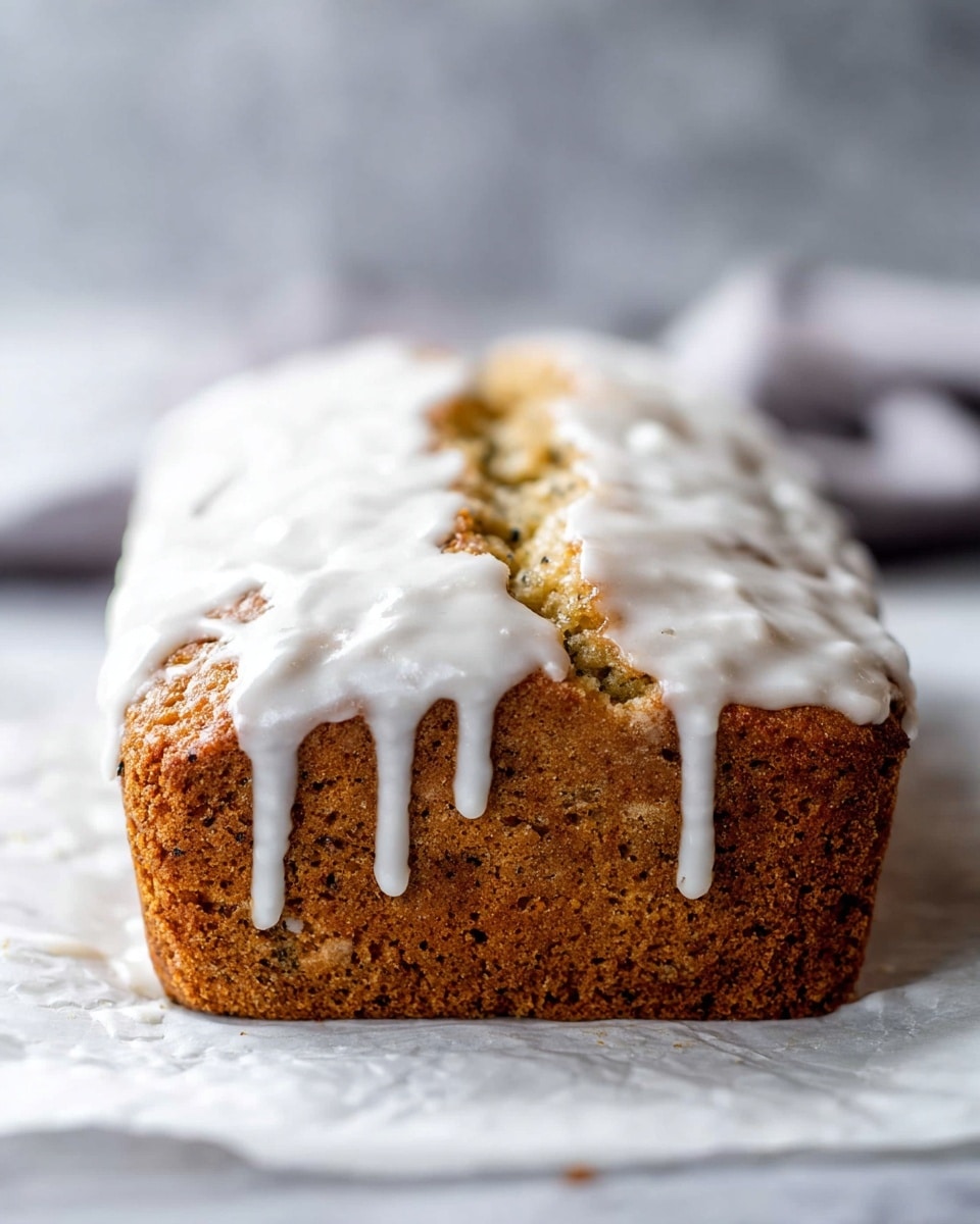 A loaf of light brown cake with small dark specks throughout, topped with a thick layer of white icing that drips down the sides in uneven, thick streams. The cake has a cracked and textured surface, showing a moist and soft inside, sitting on white parchment paper over a white marbled surface. The background is blurred with soft gray and white tones, keeping the focus on the cake. Photo taken with an iphone --ar 4:5 --v 7