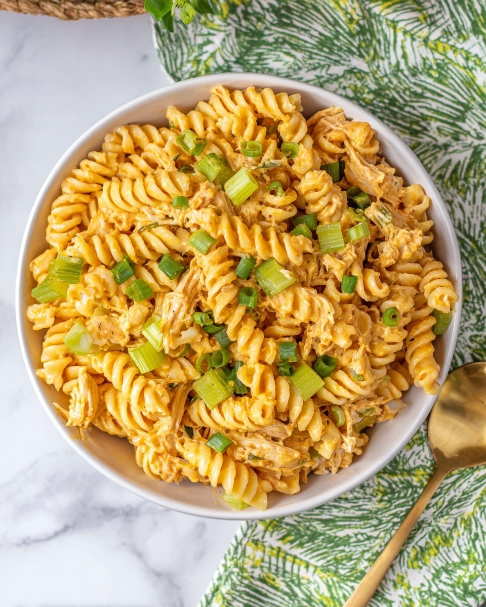 A white bowl is filled with three layers of spiraled pasta coated in a creamy orange cheese sauce. Mixed within the pasta are light green slices of celery and light brown pieces of shredded chicken, creating a textured and colorful contrast. Small chopped green onions are sprinkled evenly over the top, adding a fresh green touch. The bowl sits on a white marbled surface with a green and white patterned cloth nearby and a gold spoon to the side. Photo taken with an iphone --ar 4:5 --v 7