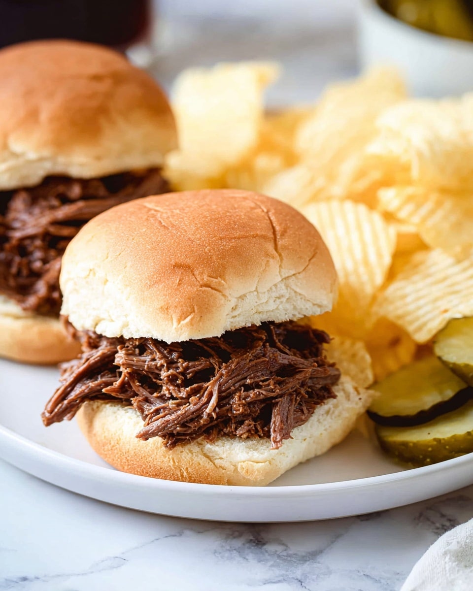 The image shows two shredded beef sandwiches on white soft buns placed on a white plate that sits on a white marbled surface. Each sandwich has one layer of finely shredded brown beef filling in the center, with the top and bottom buns resting gently on it. In the background on the plate, there is a pile of light yellow ridged potato chips. To the right side on the plate, a few greenish pickles are partially visible. The overall colors are warm and natural, with soft light highlighting the textures of the meat and bread. Photo taken with an iphone --ar 4:5 --v 7