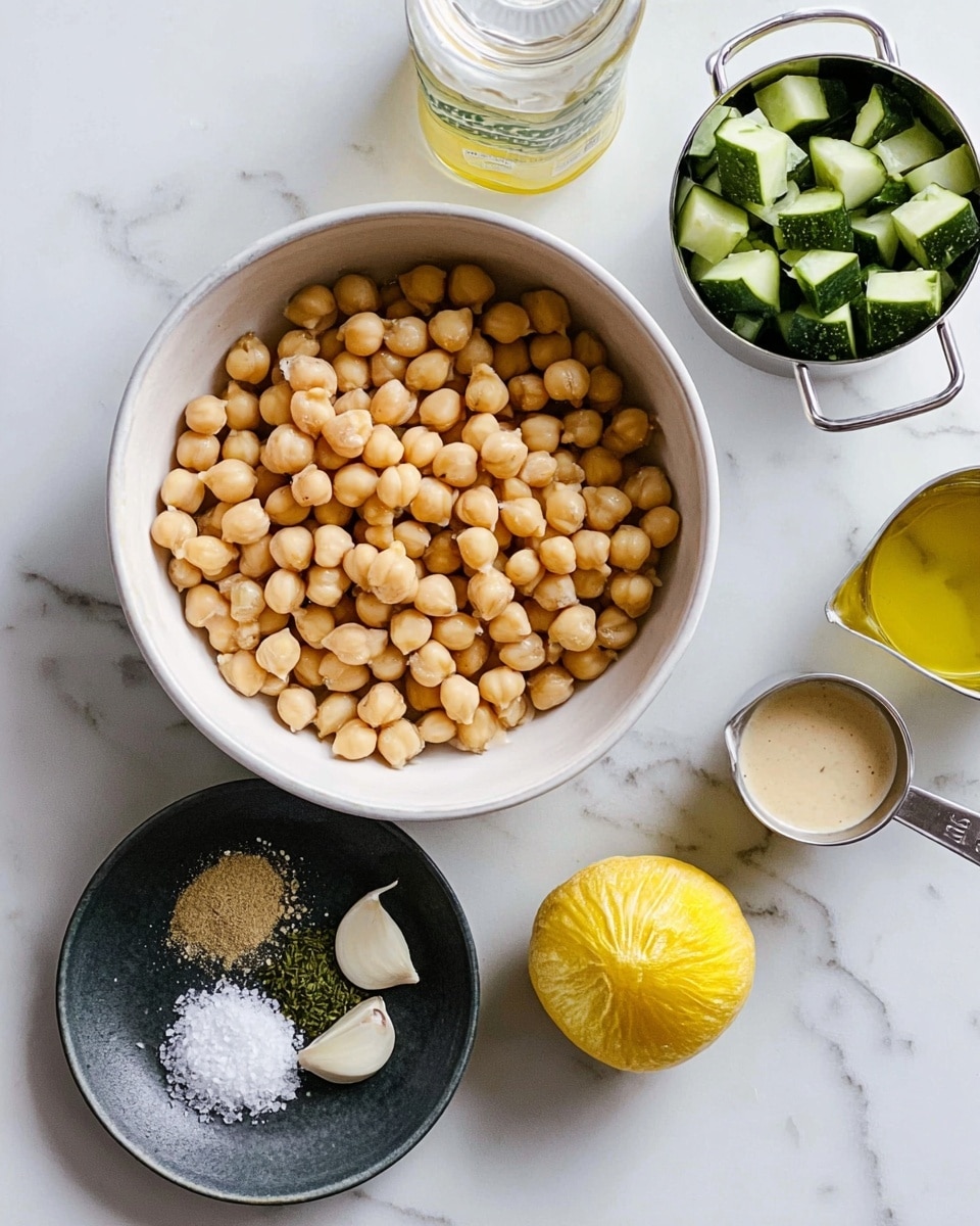 The image shows a top view of several ingredients neatly arranged on a white marbled surface. In the center, there is a white bowl filled with light beige chickpeas, round and smooth, filling it completely. At the top right, a silver measuring cup holds chunks of green cucumber with a fresh texture. To the left, a white jar contains yellow olive oil with a shiny surface. Below the chickpeas, a dark round plate holds small piles of coarse white salt, fresh green herbs, and a peeled small white garlic clove. At the bottom right, a silver measuring cup filled with creamy, off-white tahini sauce completes the setup. To the right of the chickpeas, there is a halved lemon with a bright yellow rind and juicy interior. photo taken with an iphone --ar 4:5 --v 7
