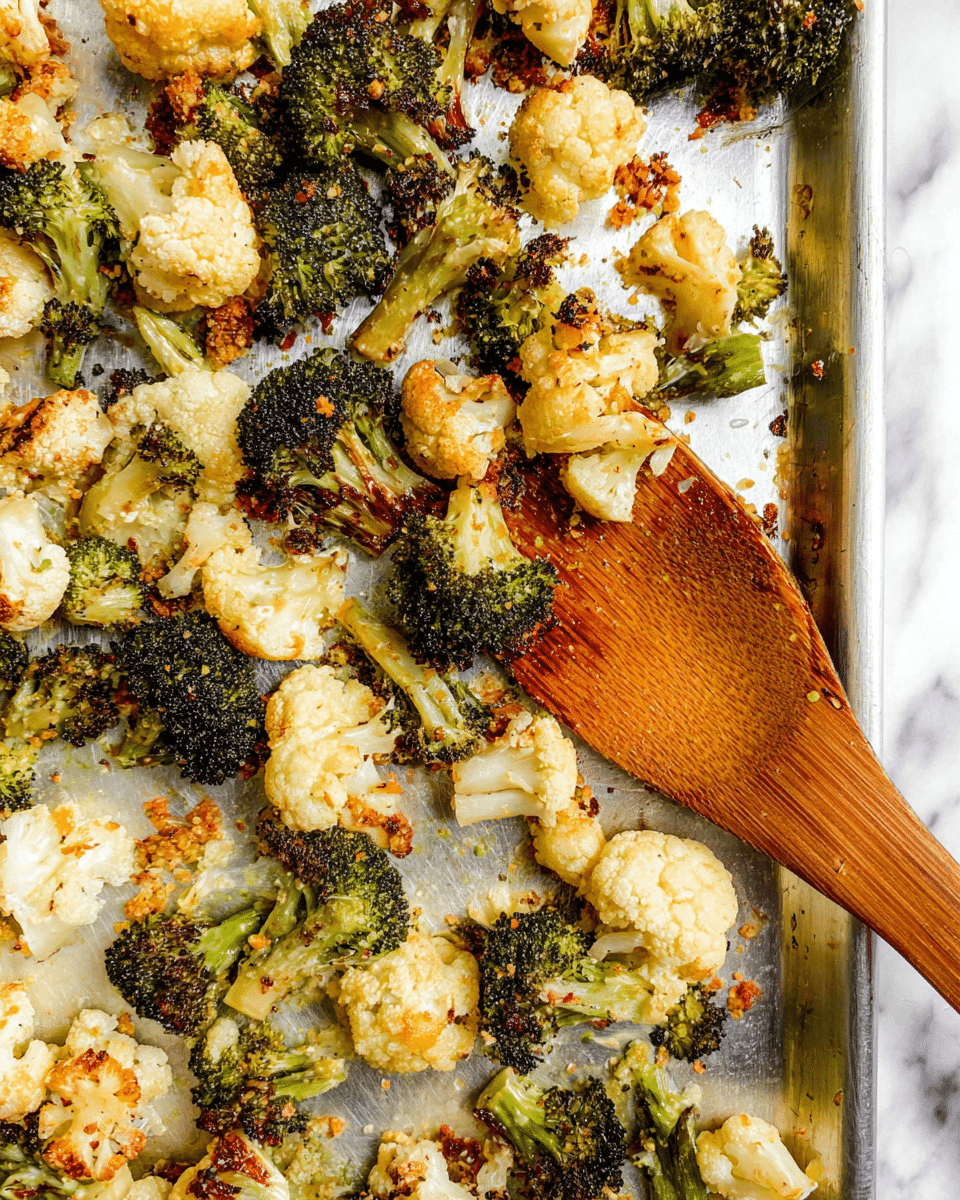 The image shows a baking tray filled with roasted broccoli and cauliflower florets. The broccoli pieces are dark green with some charred bits, giving a crispy texture, while the cauliflower parts are light cream with golden brown roasted edges. Both vegetables are scattered unevenly across the silver tray, which has slight visible marks from roasting. A wooden spatula is placed on the tray, lifting some florets with its smooth surface and rich brown color. There are small crumbs and bits of seasoning sprinkled over the vegetables, adding texture and color contrast. The background is a white marbled surface. photo taken with an iphone --ar 4:5 --v 7