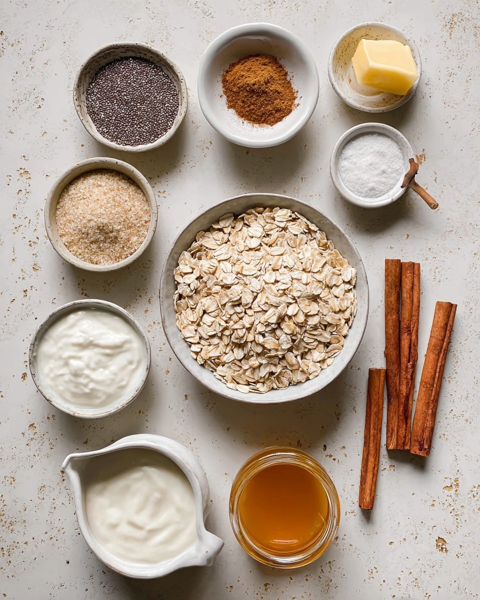 A top view of a collection of ingredients arranged on a white marbled surface: a large white bowl filled with light tan rolled oats sits near the center, surrounded by smaller white bowls holding various items. At the top left is a bowl with small dark chia seeds, next to it is a bowl with brown cinnamon powder and a small wooden spoon inside. To the right are four cinnamon sticks placed directly on the surface. Below the oats, a small bowl contains light brown sugar, a jug with creamy white liquid, and another bowl has fine white powder. At the bottom left there is a bowl with thick white yogurt, and nearby are a small amount of yellow butter in a bowl and a glass jar filled with golden syrup or honey. The arrangement is neat and well spaced. photo taken with an iphone --ar 4:5 --v 7