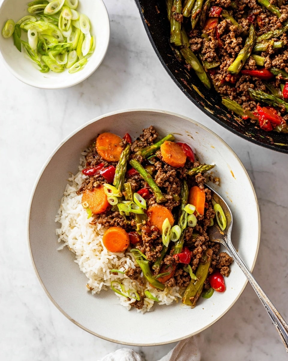 A white bowl with a layer of white rice on the right side, topped with a mix of cooked ground meat, bright orange carrot slices, green asparagus pieces, and small red bell pepper chunks spread mostly on the left side, garnished with light green sliced scallions. A silver fork rests inside the bowl on the right edge. Above the bowl to the right is a black pan containing the same mixed cooked ingredients. At the top left, there is a small white bowl with some sliced green scallions. All items sit on a white marbled surface. Photo taken with an iphone --ar 4:5 --v 7