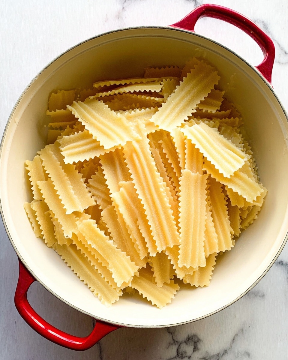 Long, narrow pasta strips with wavy edges are stacked closely together inside a large white pot with red handles. The pasta pieces are pale yellow with a slightly rough texture. The pot sits on a white marbled surface with faint gray veins running through it. The light source comes from above, casting soft shadows on the pasta and inside the pot. photo taken with an iphone --ar 4:5 --v 7