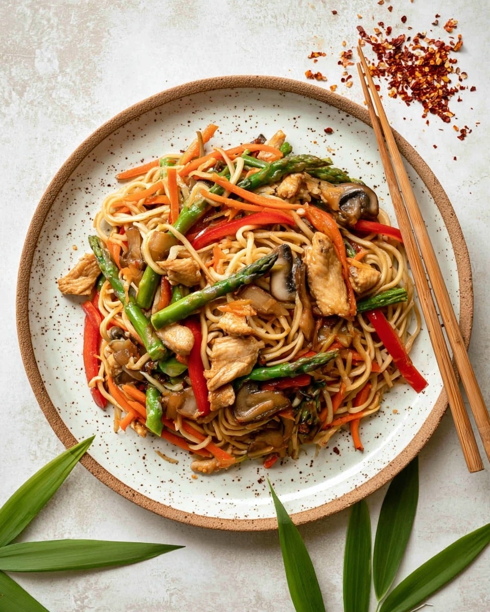 A round white speckled plate is filled with a colorful stir-fry layered as follows: the bottom layer is light brown noodles twisted around each other, topped with bright orange carrot strips, green asparagus pieces, sliced brown mushrooms, and red bell pepper strips. Scattered on top are small, light brown chunks of chicken. The plate sits on a white marbled surface with a pair of wooden chopsticks placed vertically to the right. Green bamboo leaves decorate the corner of the scene, with some crushed red chili flakes scattered near the plate. Photo taken with an iphone --ar 4:5 --v 7