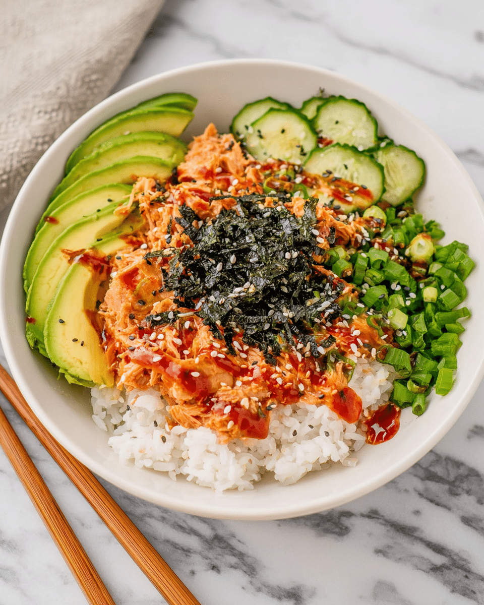 A white bowl filled with a base layer of white rice at the bottom, topped with several sections: thinly sliced avocado fanned out on the left side, green chopped scallions beside the avocado, cucumber slices behind the scallions, shredded orange-colored chicken or tuna with a sauce drizzled over it on the right, and a generous sprinkle of black seaweed flakes and white sesame seeds in the center. The dish is dressed with a reddish sauce drizzled over the top, creating a colorful and textured mix. The bowl sits on a white marbled surface, with wooden chopsticks placed beside it. Photo taken with an iphone --ar 4:5 --v 7