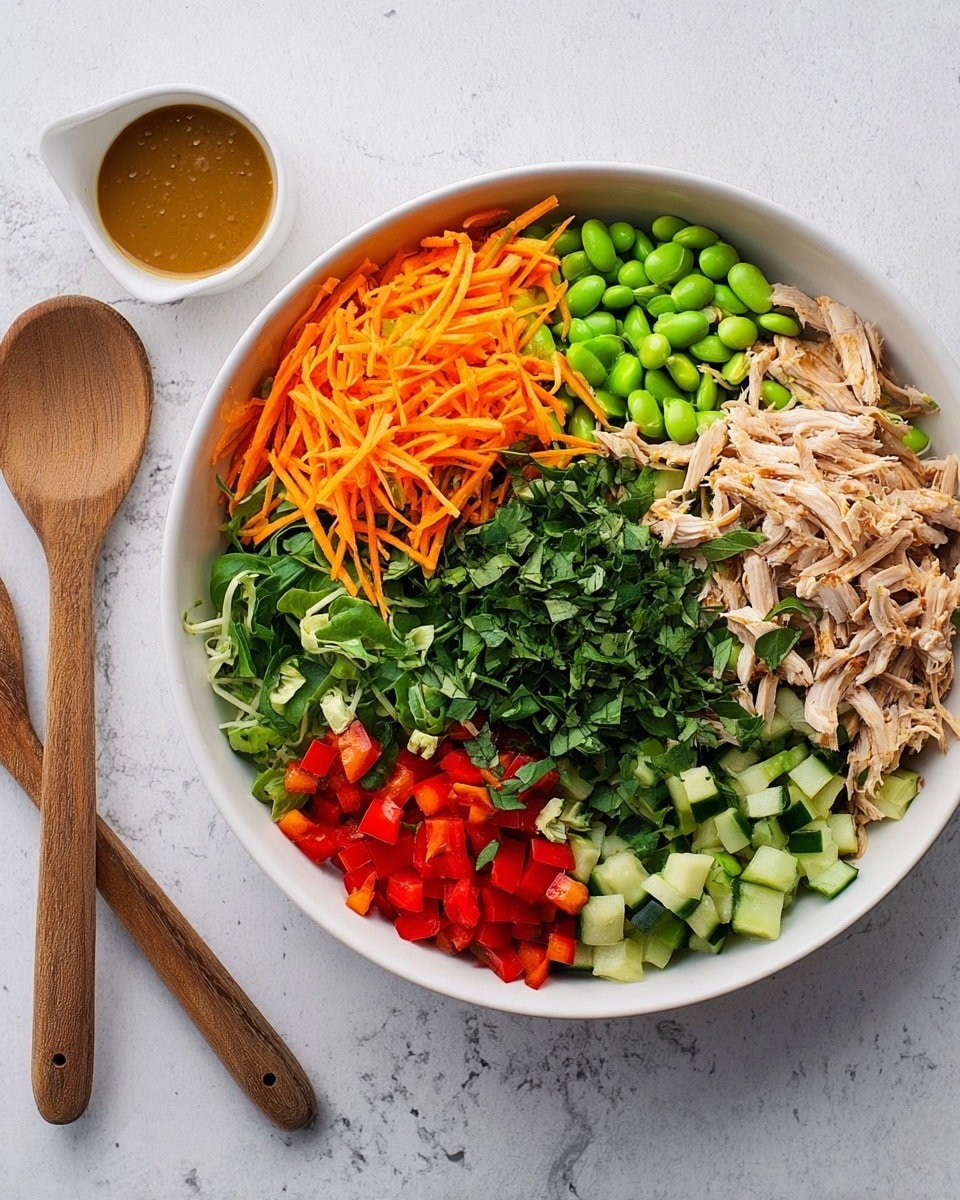 A white bowl filled with a colorful salad arranged in sections. Starting from the top left and moving clockwise, there are bright orange shredded carrots, green edamame beans, shredded light brown chicken, light green cucumber chunks, red bell pepper pieces, and chopped dark green herbs covering the center. Next to the bowl, on the white marbled surface, is a small white bowl with brown salad dressing and two wooden salad serving utensils. Photo taken with an iphone --ar 4:5 --v 7