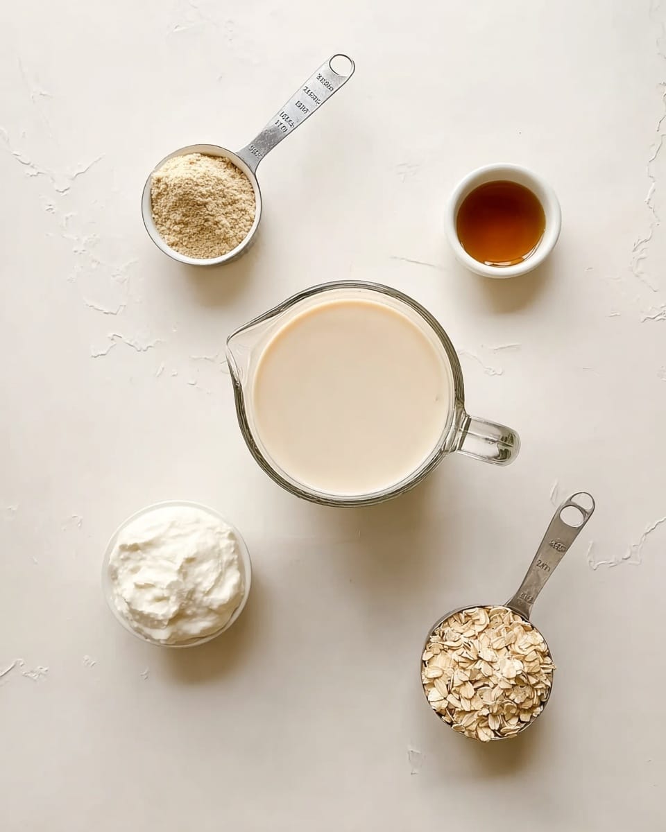 A top-down view of a clear glass pitcher filled with light beige creamy liquid placed at the center on a white marbled surface. Around the pitcher, four small white bowls and measuring cups are spaced evenly: at the top left is a metal measuring cup filled with light brown powder, at the top right is a white bowl with a small amount of dark amber liquid, at the bottom left is a white bowl filled with thick white cream, and at the bottom right is a metal measuring cup filled with light brown oats. The scene is simple and clean, with soft natural light highlighting the smooth textures. Photo taken with an iphone --ar 4:5 --v 7